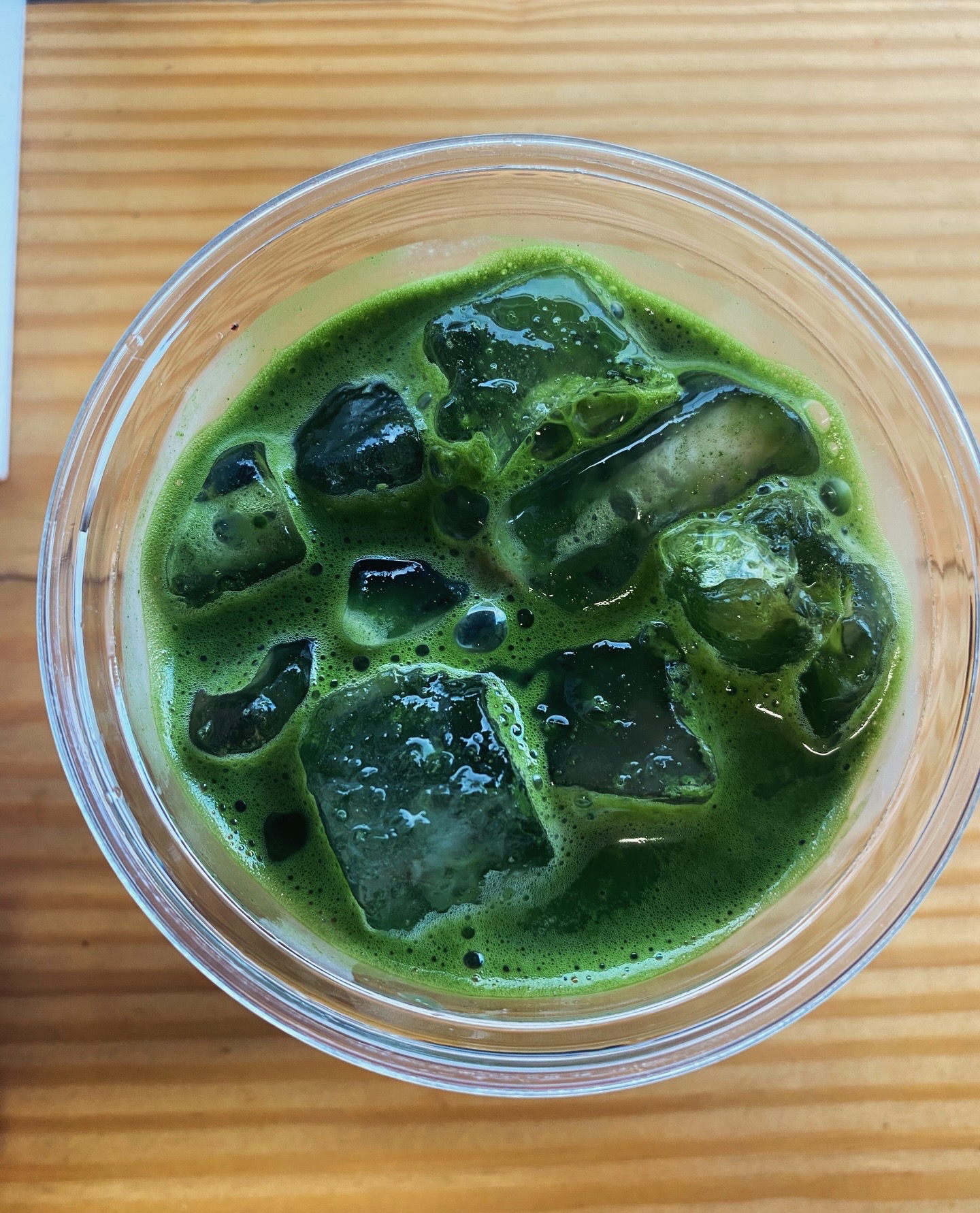 Green jelly-like cubes in a clear cup with green liquid, on a wooden surface.