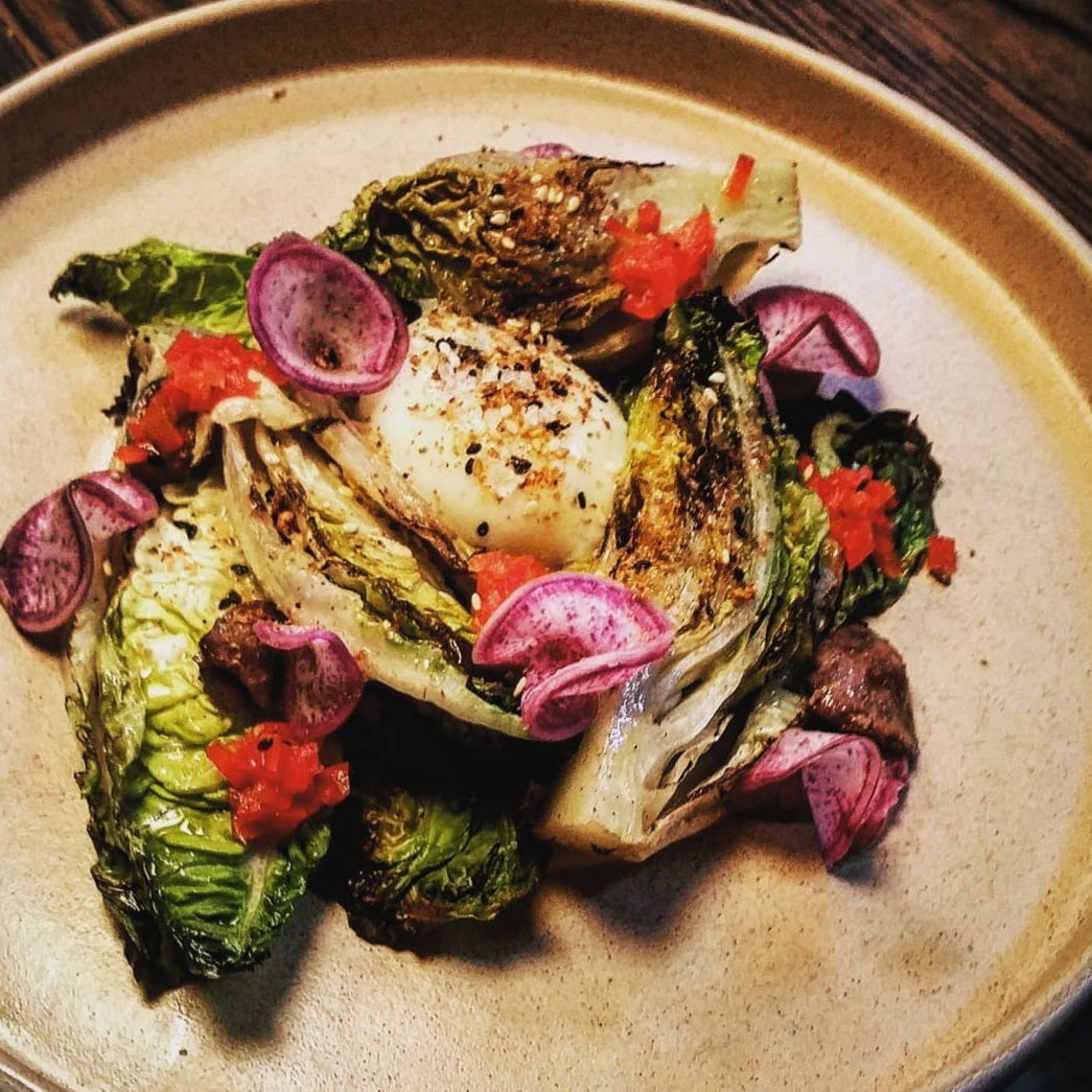 Grilled romaine lettuce with purple onion slices and red garnish on a beige plate.