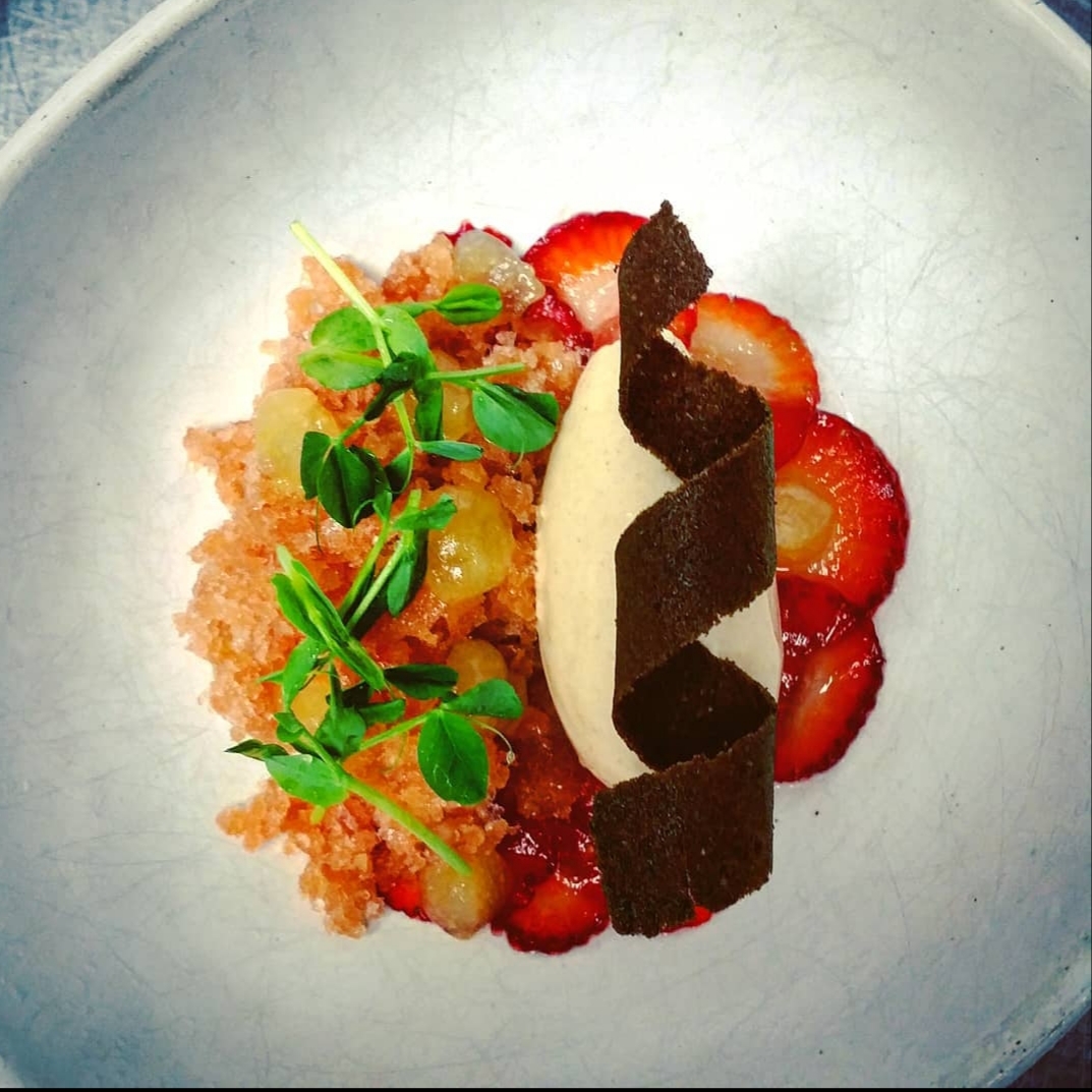Dessert with strawberries, cream, chocolate pieces, and green garnish on a white plate.