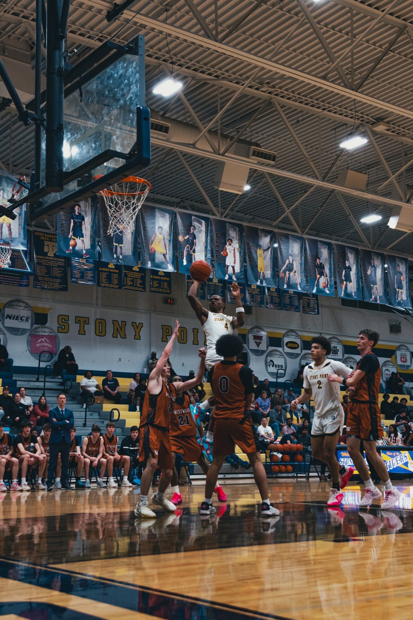 Basketball game with players jumping for the ball, spectators watching, and banners hanging in the gymnasium.