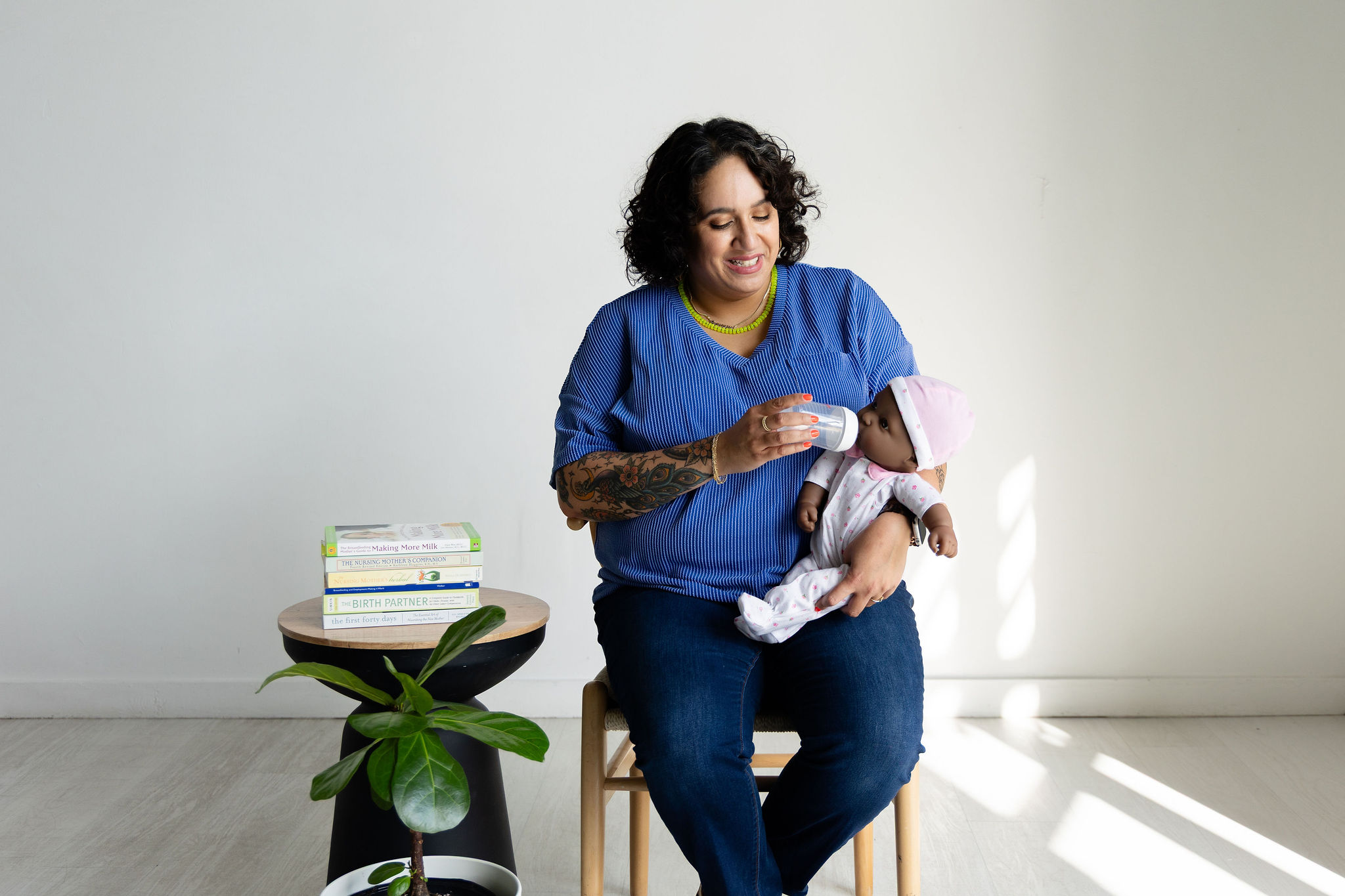 Woman sitting on a chair holding a baby, with a small table and a plant nearby, in a bright room.