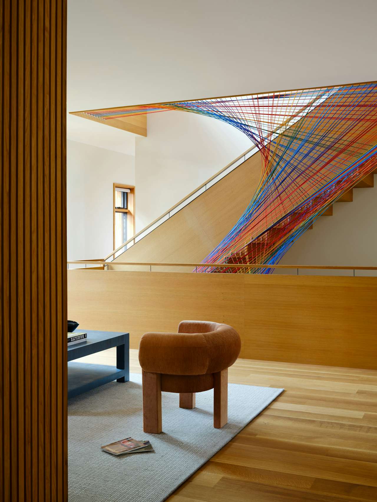 Interior space with a colorful abstract art installation on the staircase wall, wooden flooring, and a small seating area with a brown stool.
