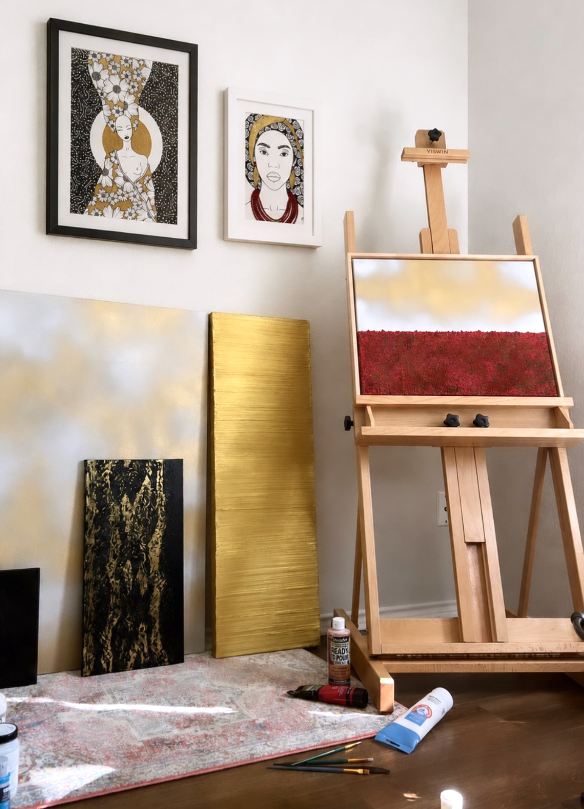Art studio with paintings, easel, and supplies, against a white wall, with a colorful rug on the floor.