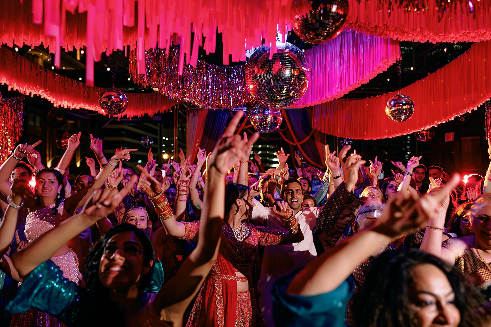 Crowd of people dancing at a party with colorful decorations and hanging ornaments, vibrant lighting, and festive atmosphere.