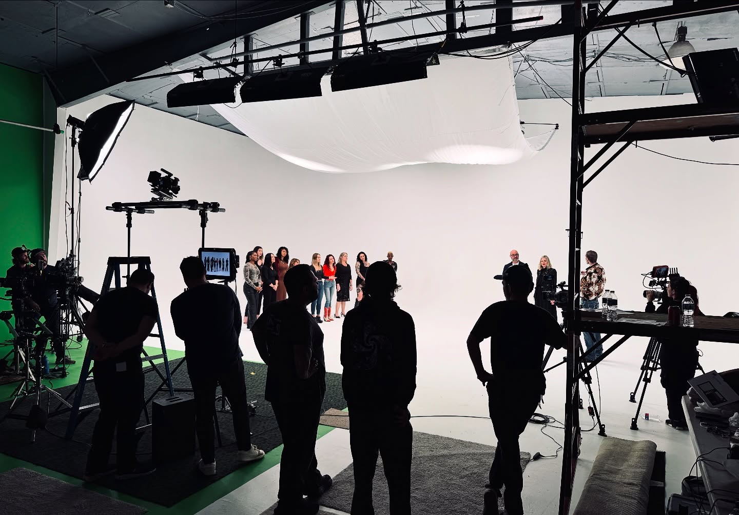 Film production studio with crew, cameras, and lighting equipment in front of a white backdrop.