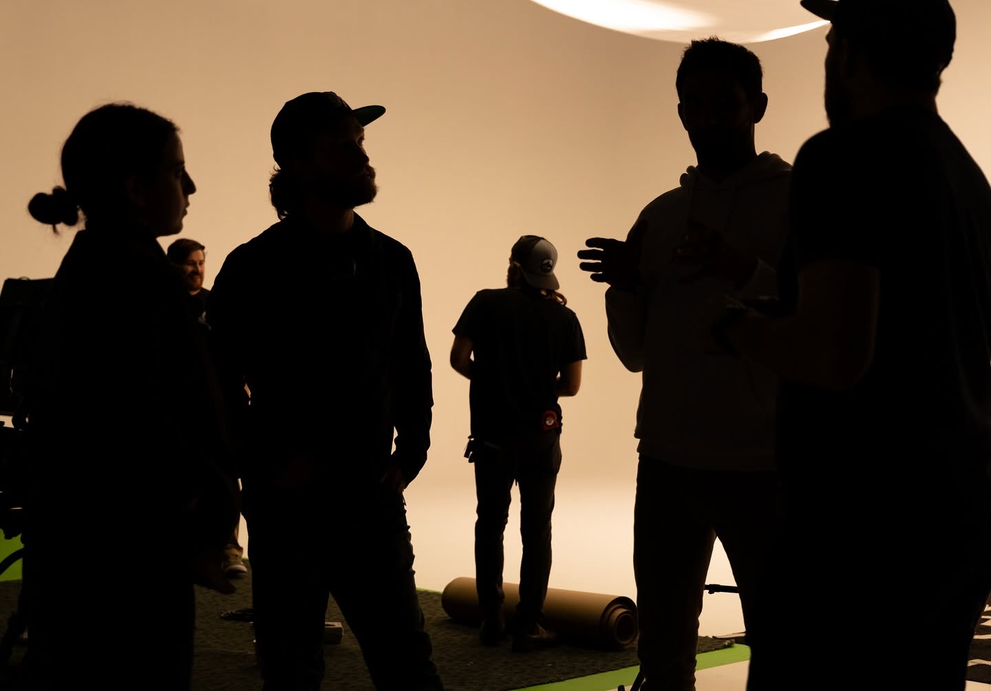 Silhouettes of people standing and talking indoors, with a light background and some objects on the floor.