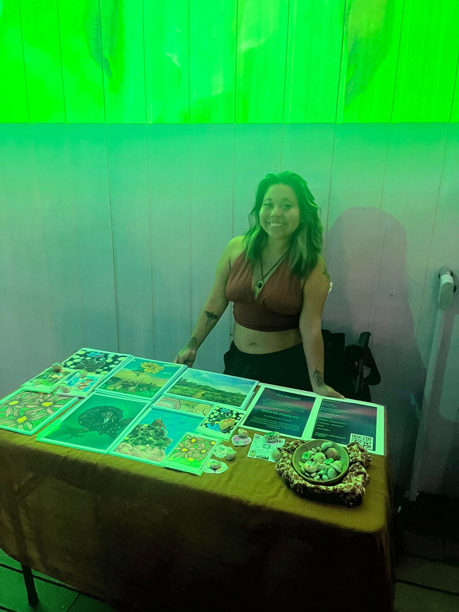 Woman standing next to a table with colorful comic book pages, in a room with green lighting.