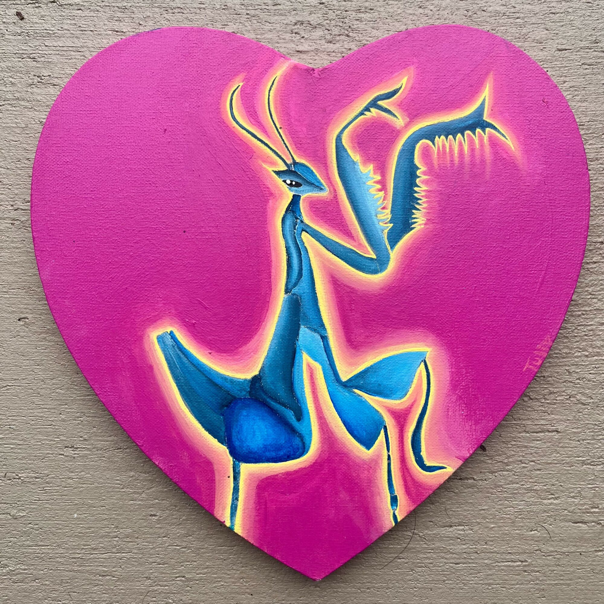 Pink heart-shaped object with a stylized blue creature holding a plant, on a wooden surface.
