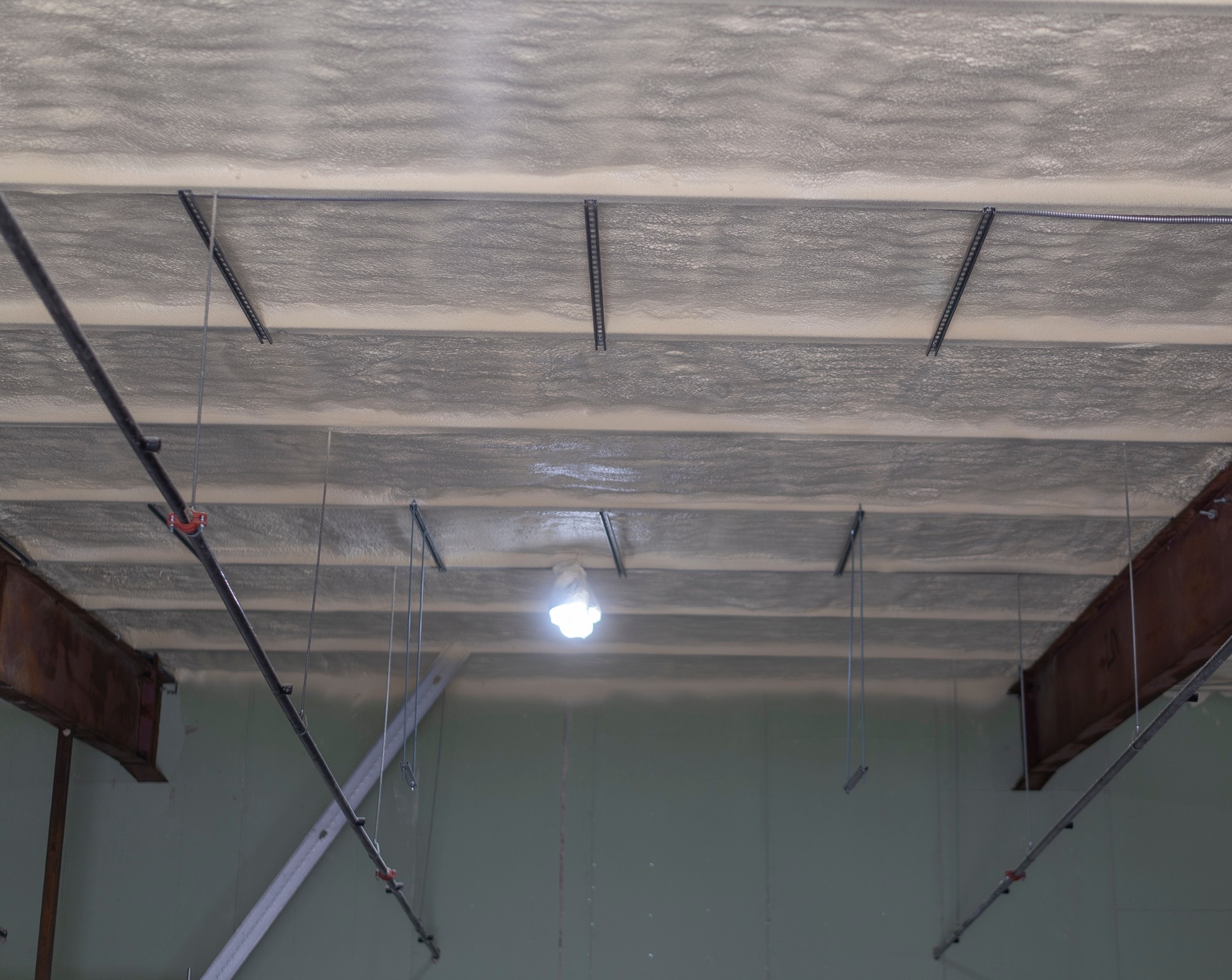 Ceiling with insulation and support beams, light fixture, and hanging wires, viewed from below.
