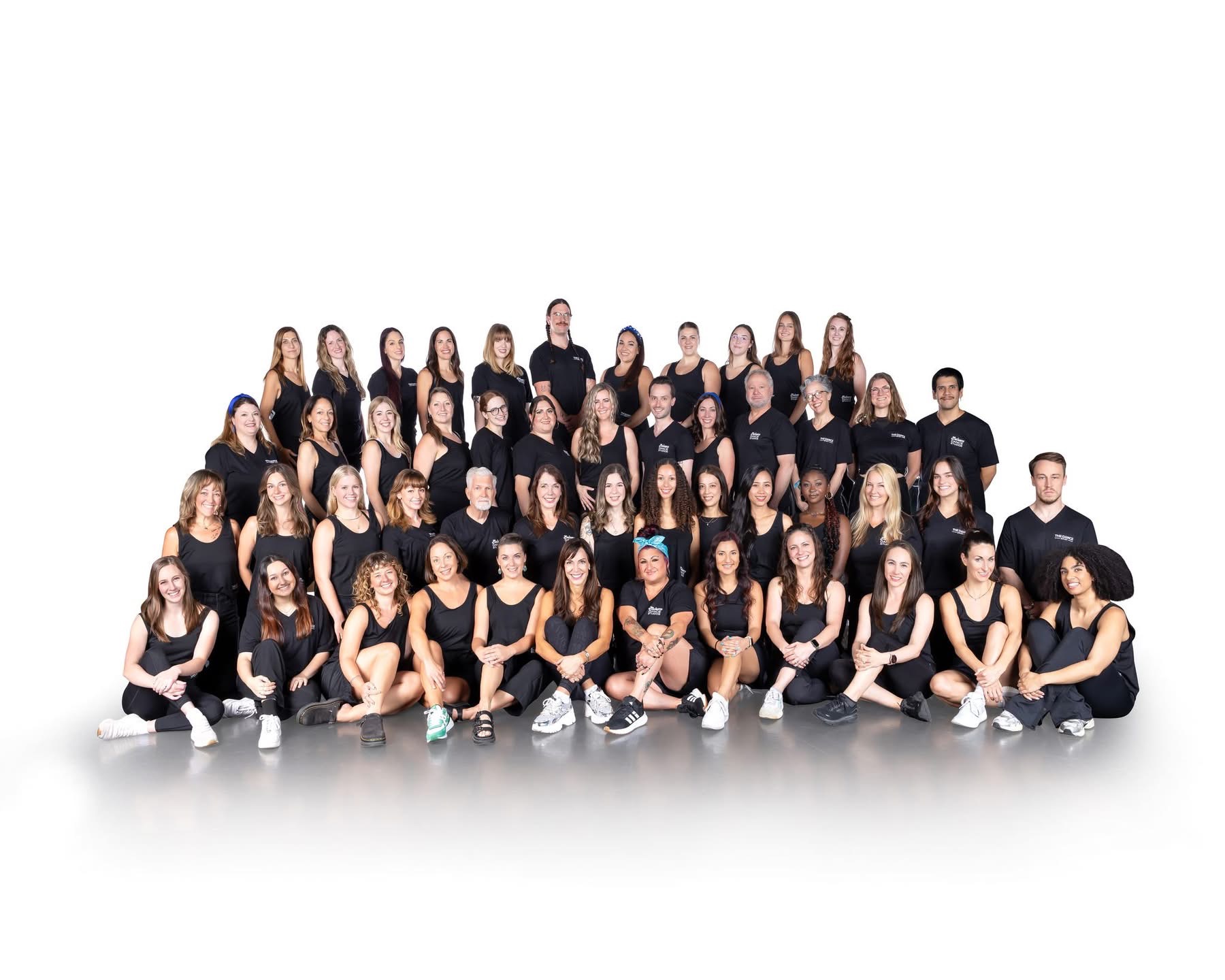 Group of people in black clothing standing and kneeling, posing for a photo against a white background.