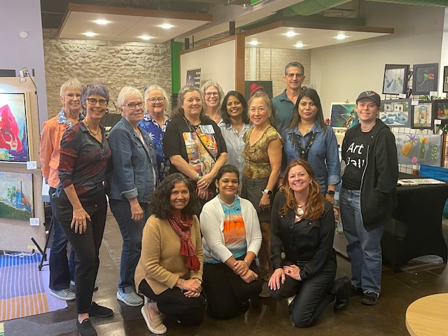 Group of fifteen people standing indoors, some smiling, in front of artwork and display cases.