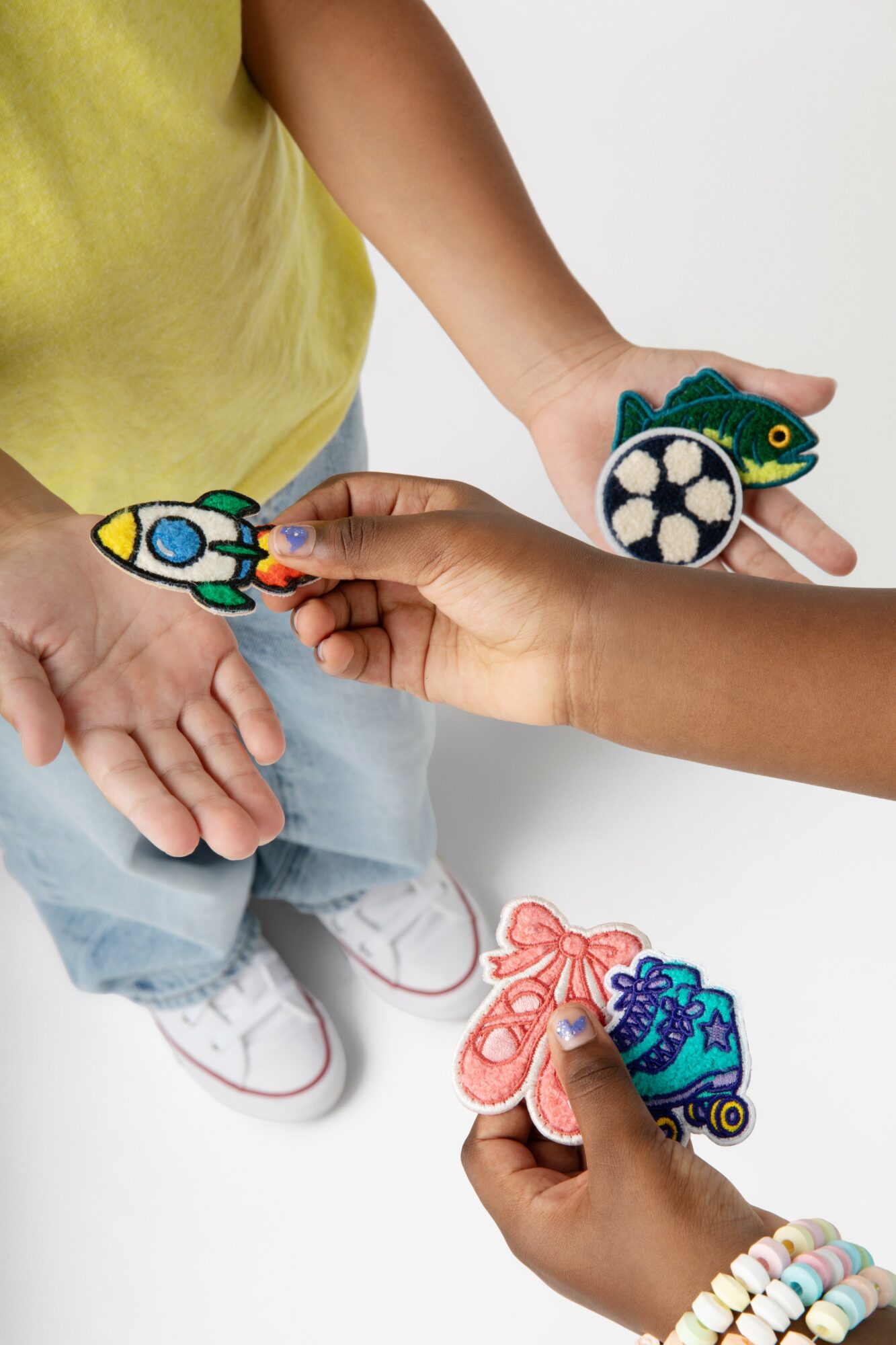 Two children hold colorful felt rocket and spaceship puppets, with one child wearing a yellow shirt and light blue pants.