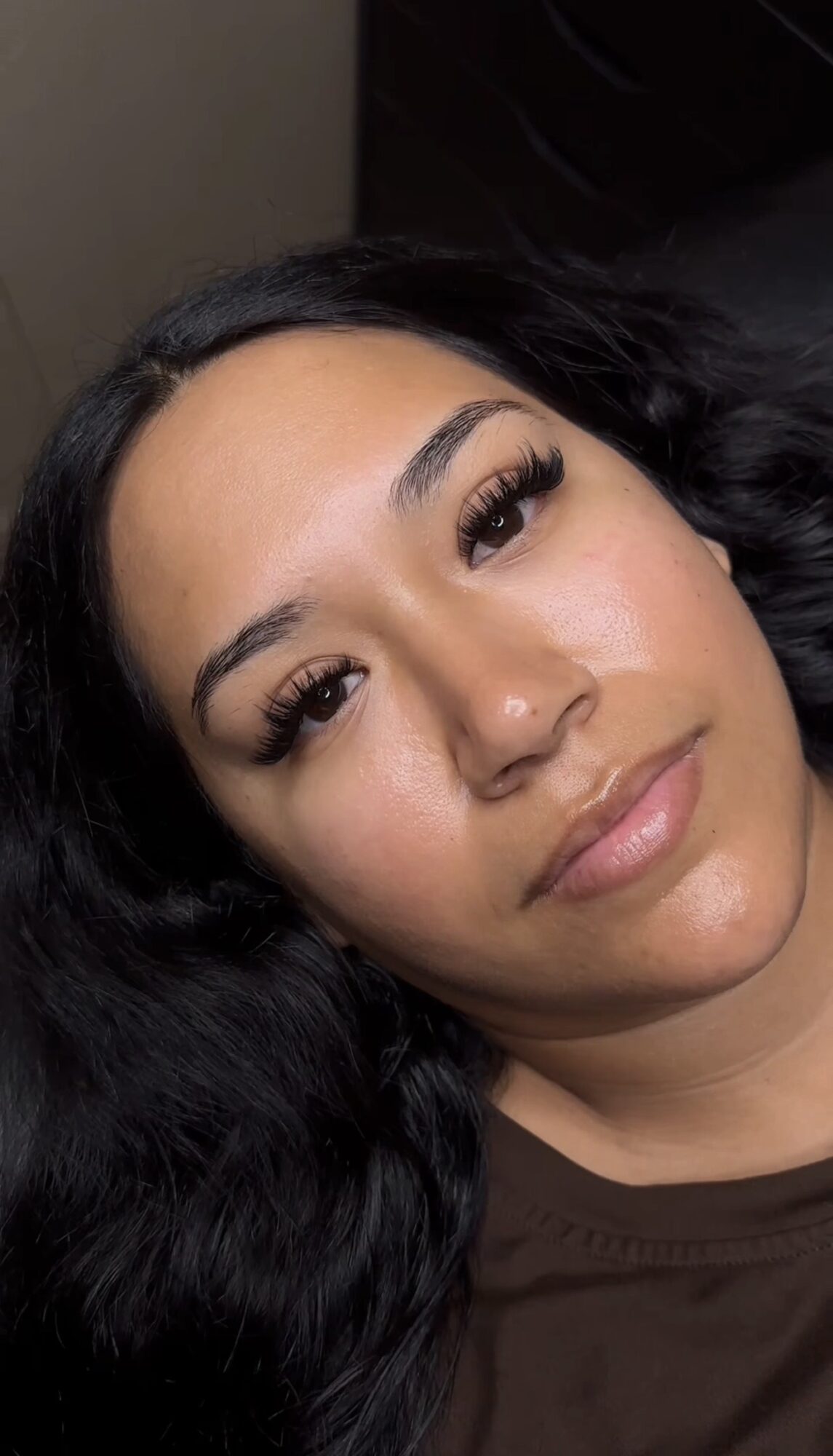Close-up of a woman with long dark hair, makeup, and a neutral expression, lying down.