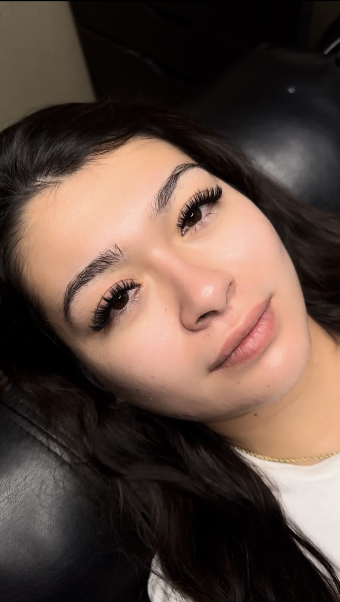 Close-up of a woman with long dark hair, lying on a black surface, looking at the camera with a neutral expression.