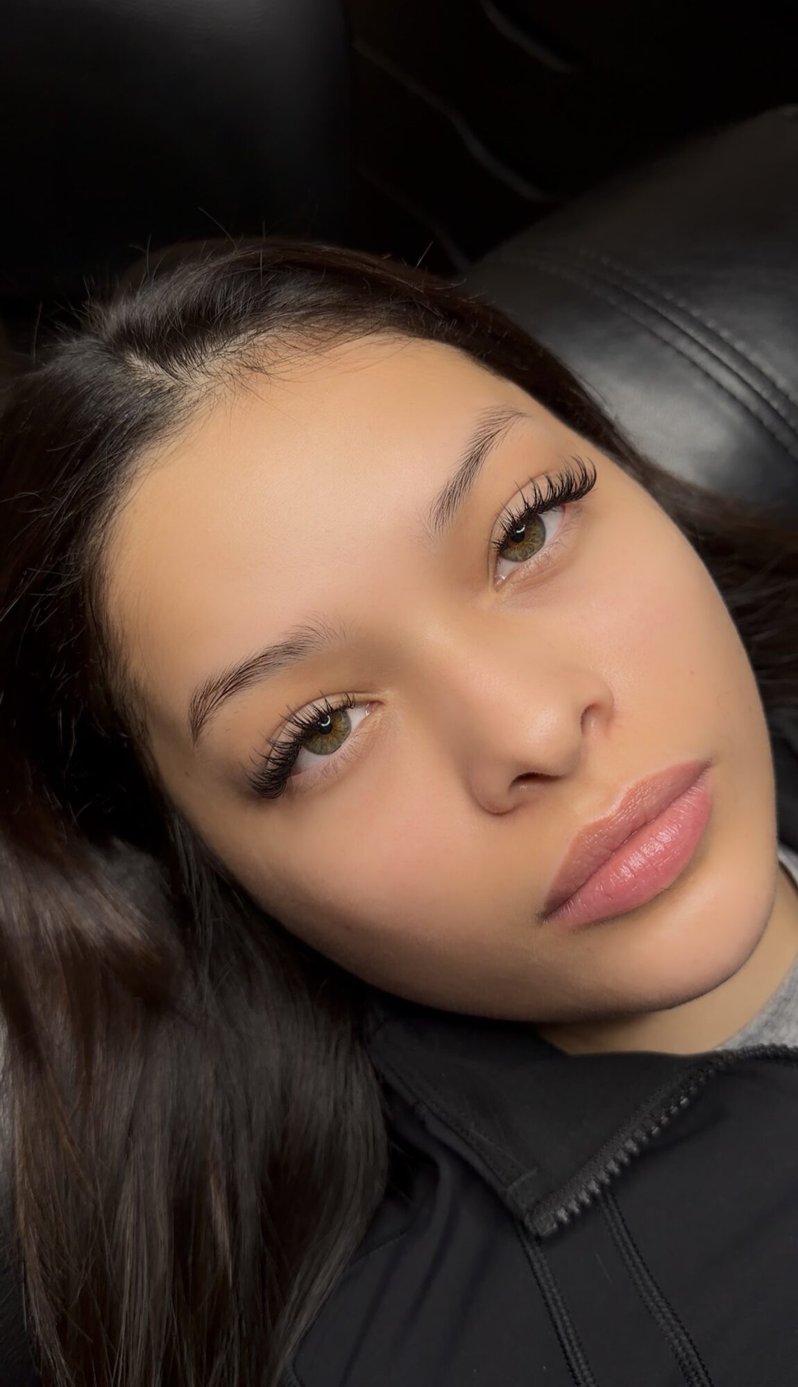 Close-up of a young woman with long dark hair, lying down, looking at the camera, with neutral expression.