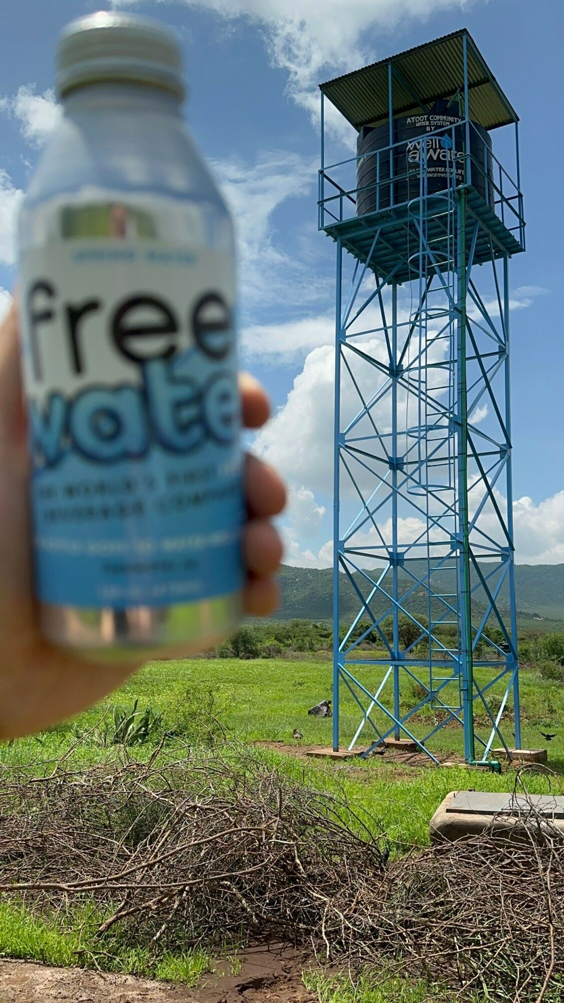 Person holding a bottle of Frescolate in front of a tall metal tower with a platform, green grass, and blue sky.