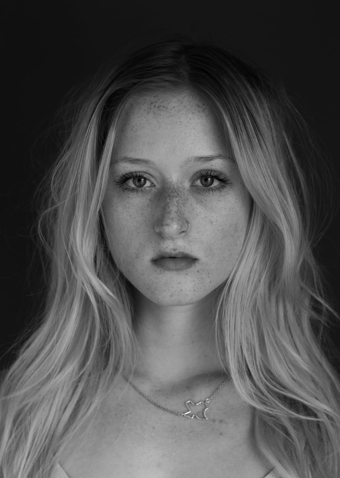 Portrait of a young woman with long, wavy hair and freckles, looking directly at the camera, black background