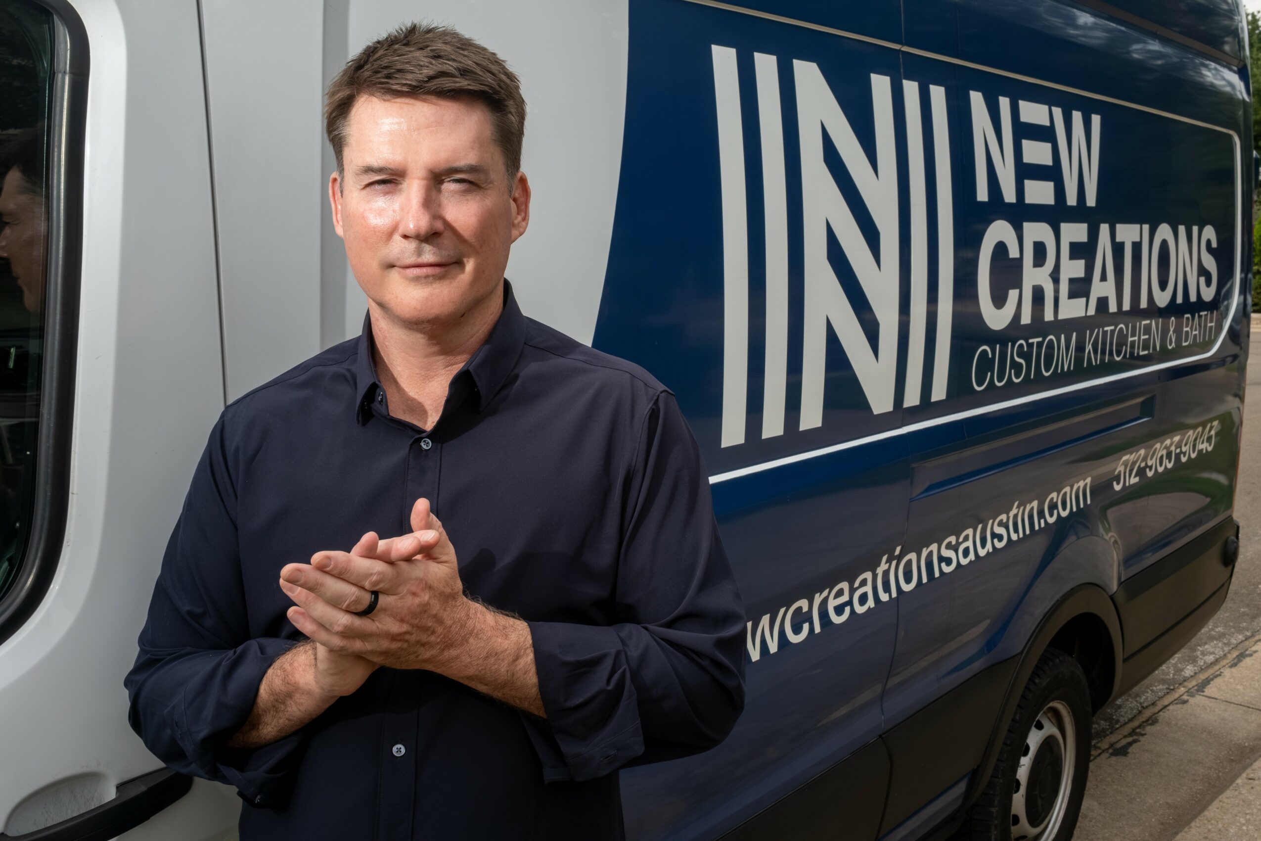 Man with short hair and dark shirt standing in front of a van with company logo and website.