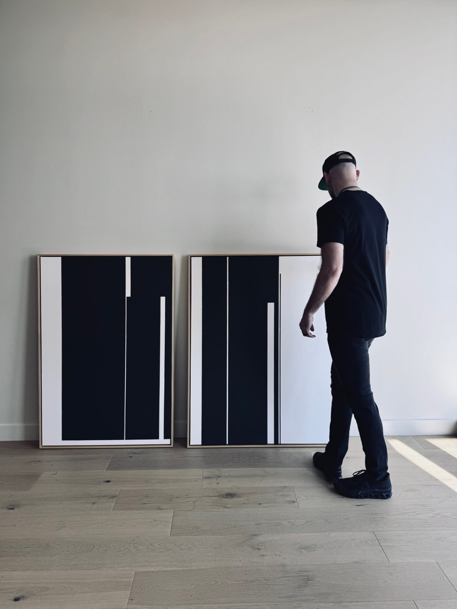 Person standing next to two black and white cabinets against a plain wall, looking down, wearing a black shirt and jeans.