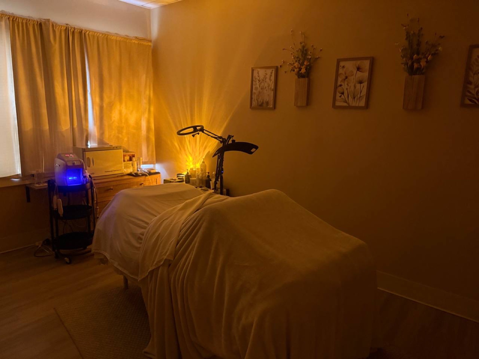 Room with a massage table, bicycle, and a desk with a blue lamp, warm lighting, and wall decorations.