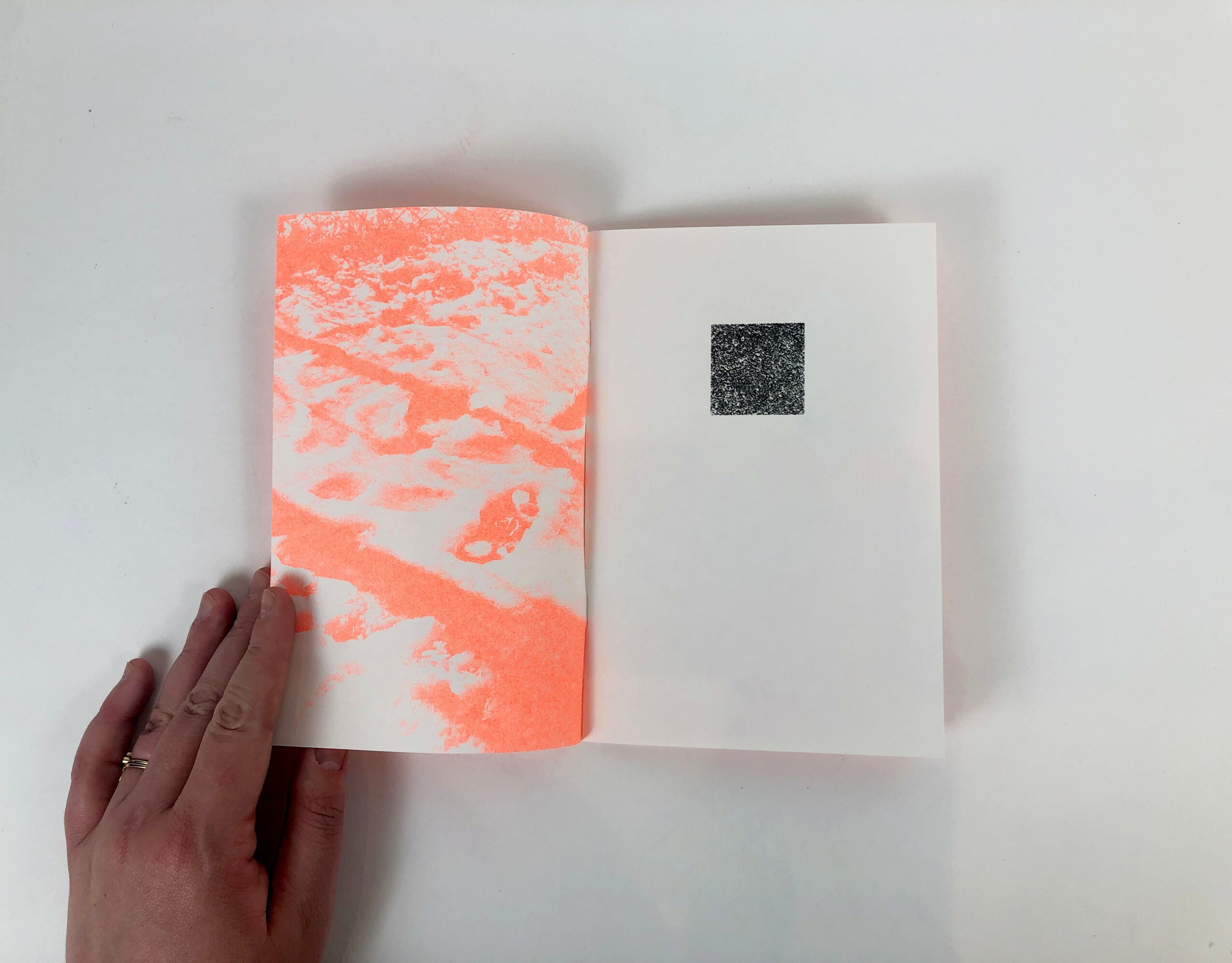 Open book with a black square on the right page, and a pink and white abstract pattern on the left page.