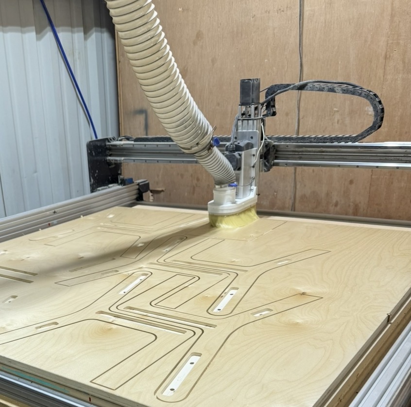 A CNC machine with a robotic arm and a vacuum tool working on a wooden surface with engraved lines.