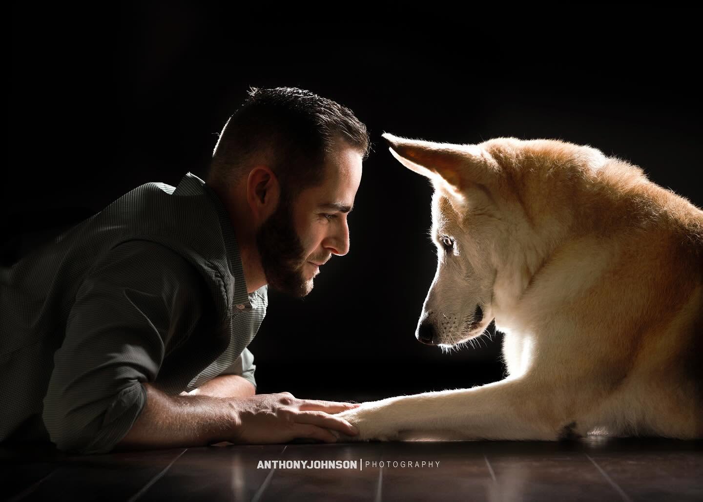 Man and dog face each other closely in a dark setting, with light highlighting their faces and paws touching.