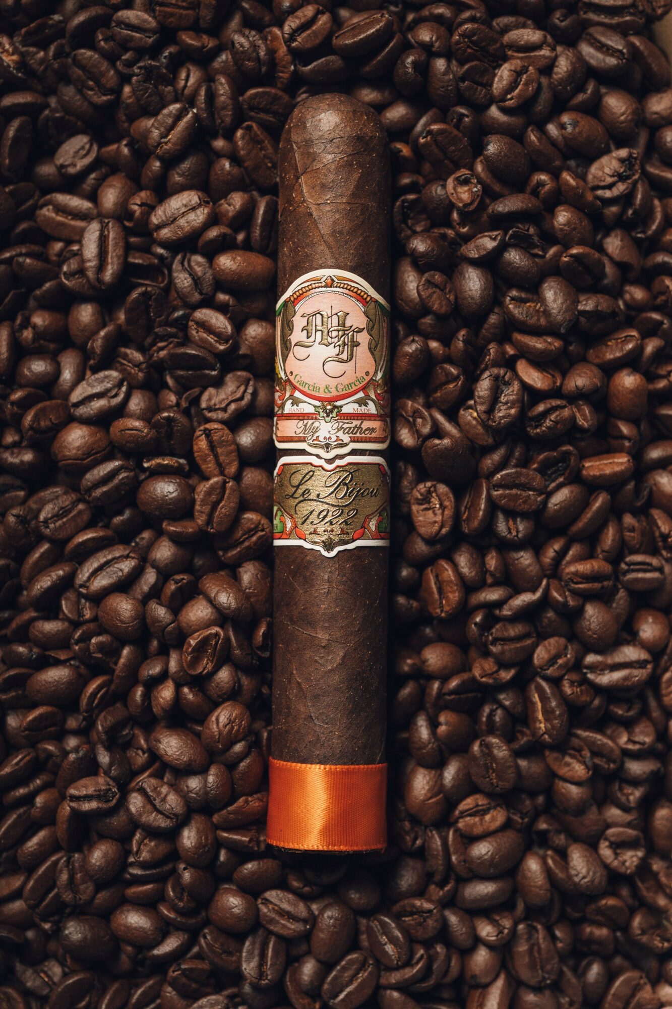 Cigar placed on a bed of roasted coffee beans, with a decorative band and orange tip.