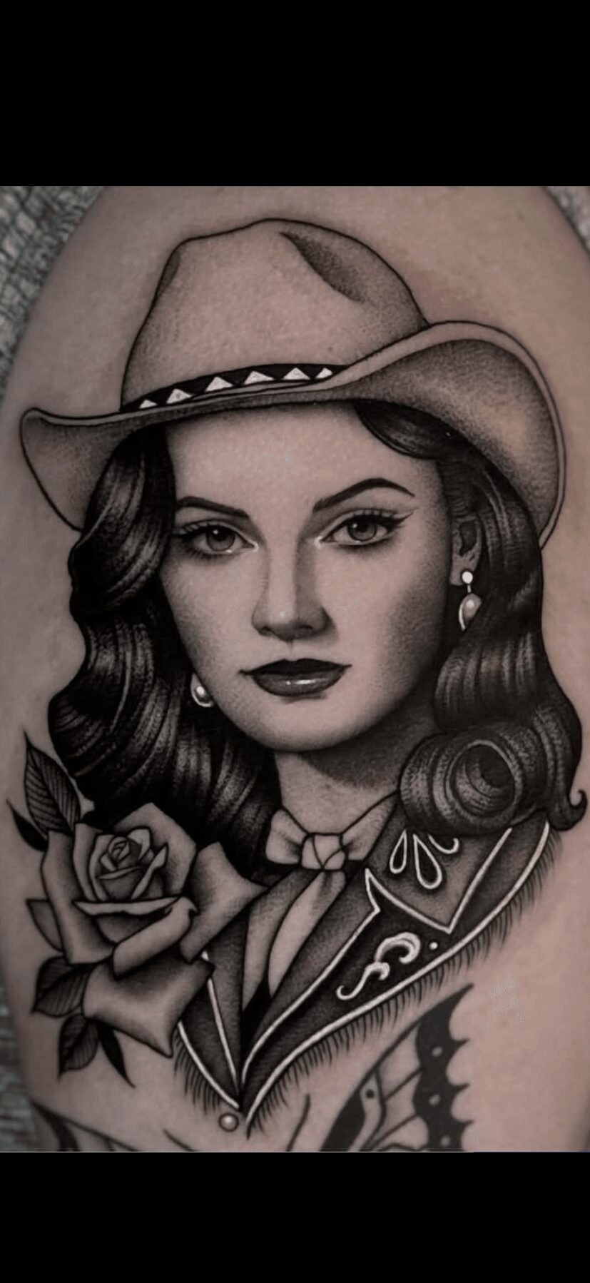 Black and gray tattoo of a woman wearing a cowboy hat, with long hair, a rose, and decorative elements.