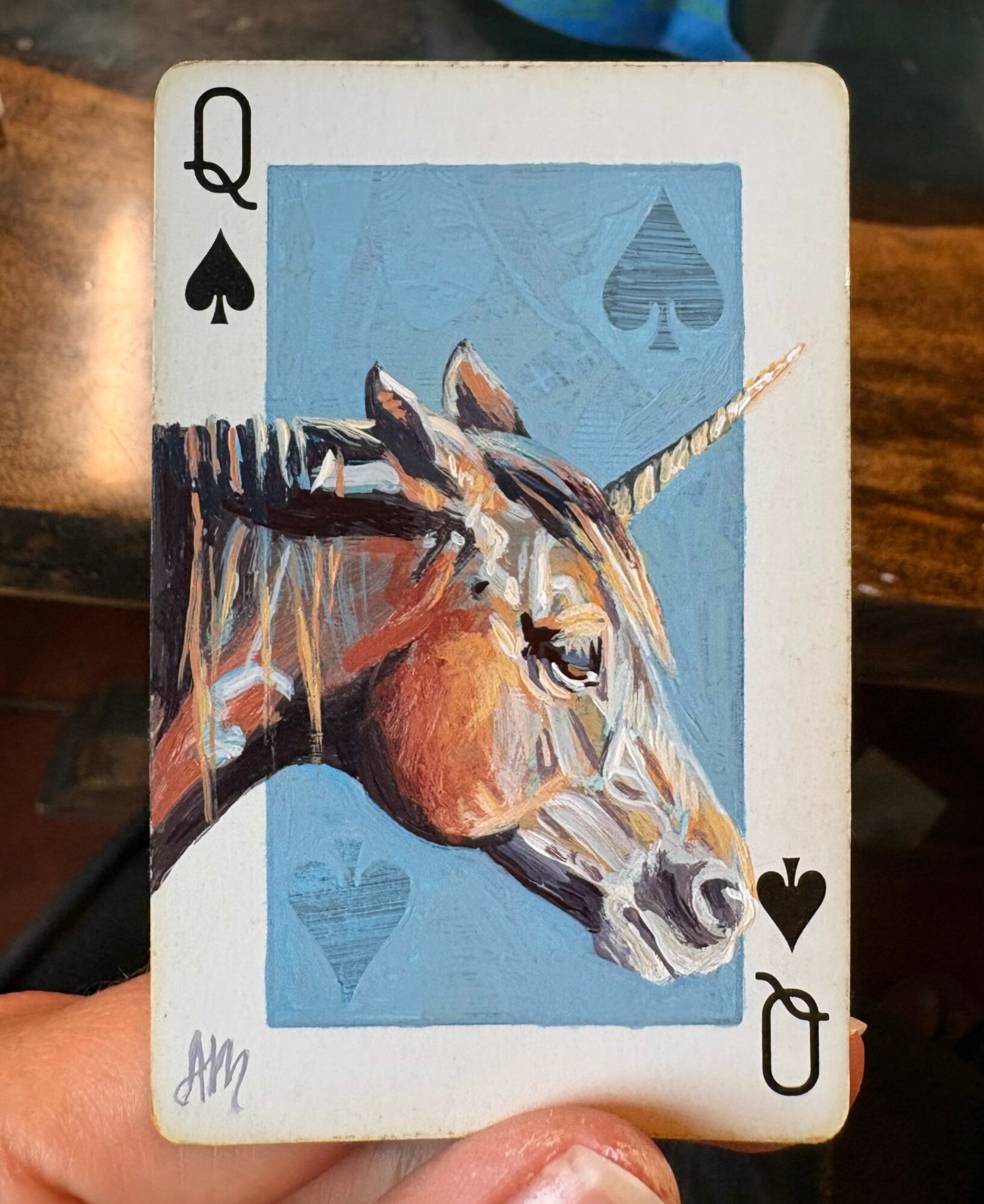 Playing card Queen of Spades featuring a unicorn illustration with a blue background and spade symbols.