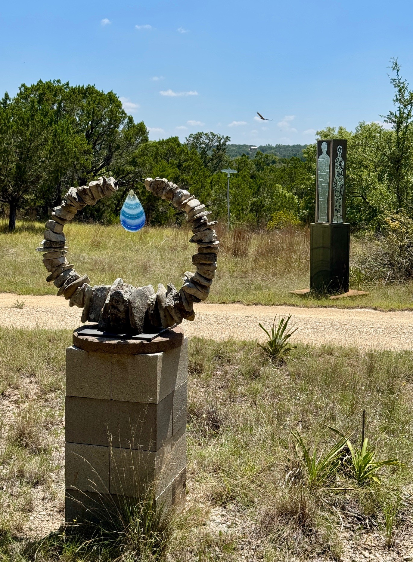 Stone sculpture with a blue and white striped egg in a natural outdoor setting, trees, and a sign in the background.