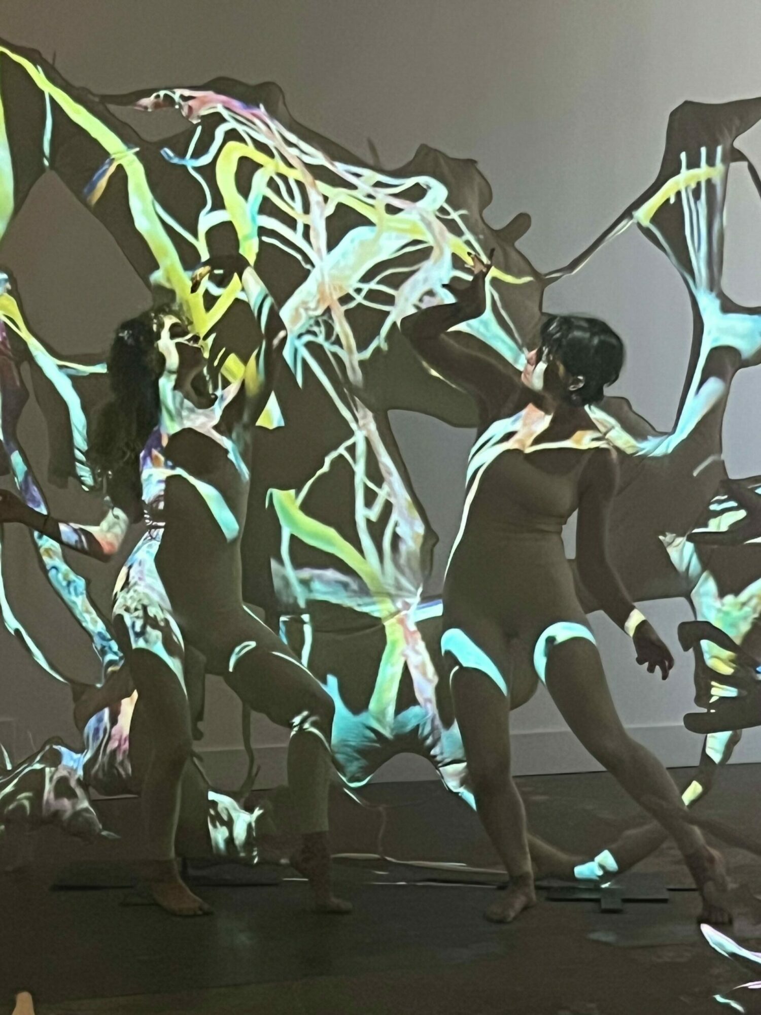 People performing a dance or performance with glowing, colorful body paint or costumes, on a dark stage or room.