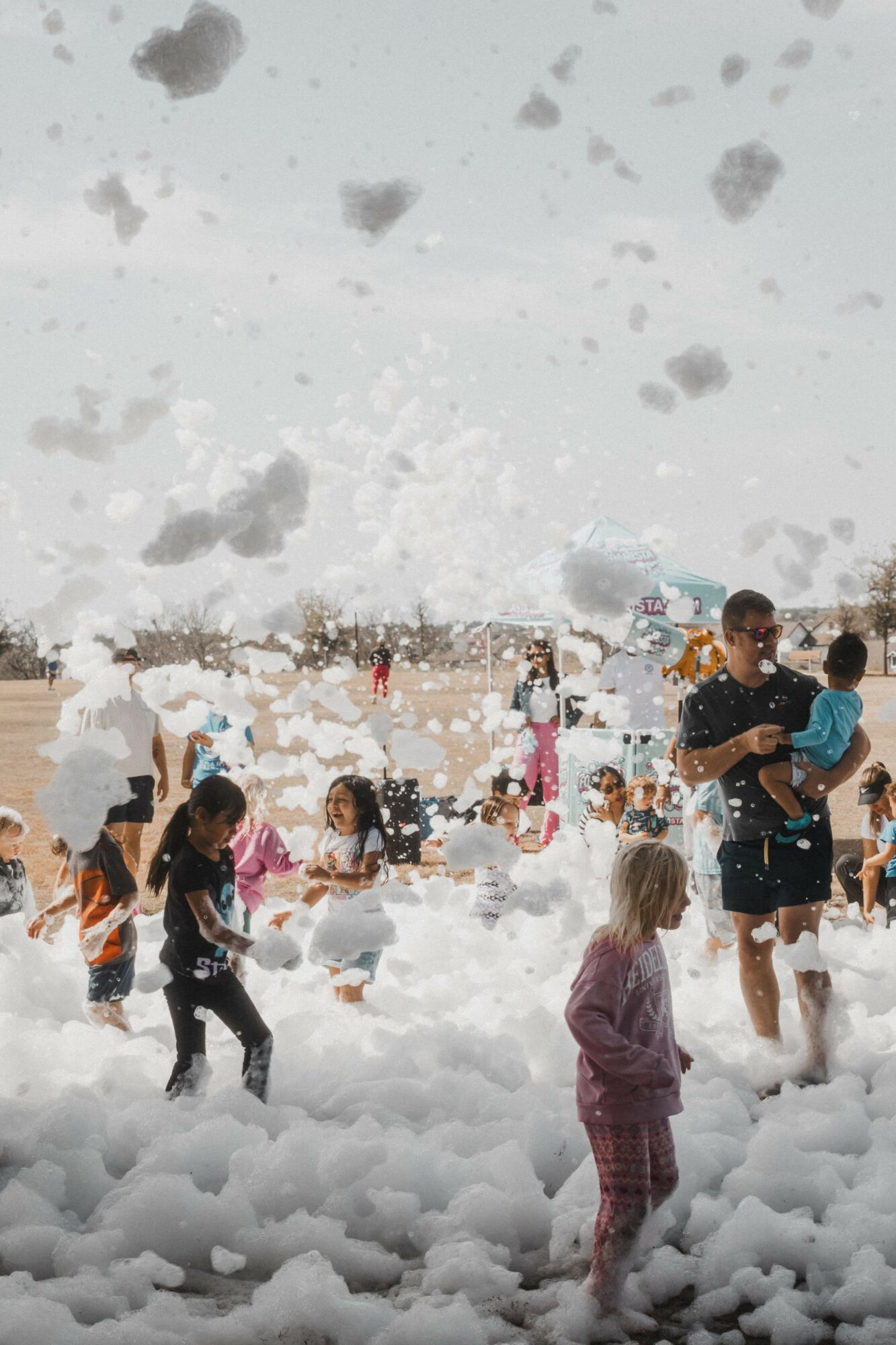 Children and adults playing in snow outdoors, some children are running and others are standing, with a person holding a child.