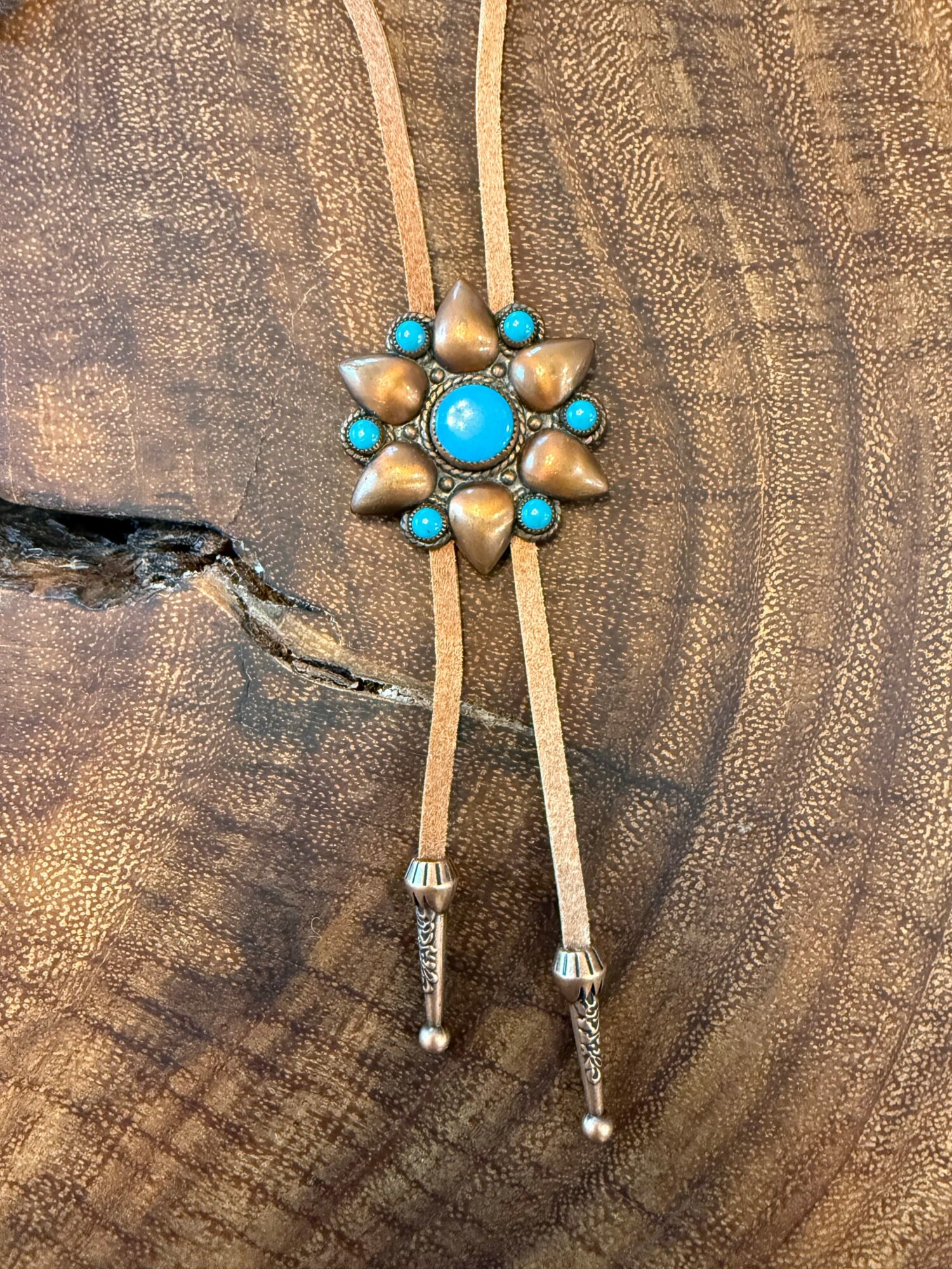 Decorative jewelry piece with a central turquoise stone surrounded by smaller turquoise and metallic beads, on a wooden surface.