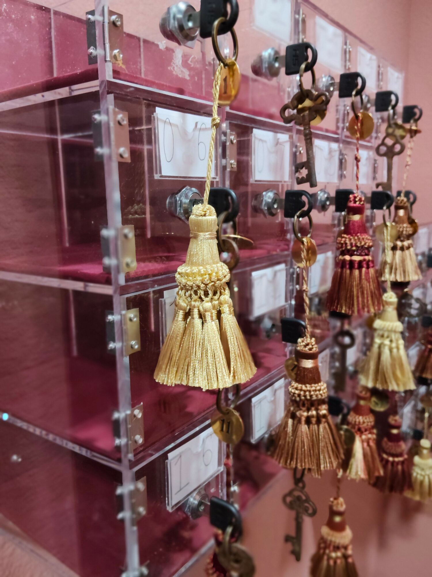 Display of decorative tassels with beads hanging from hooks, arranged on a transparent stand against a pink background.