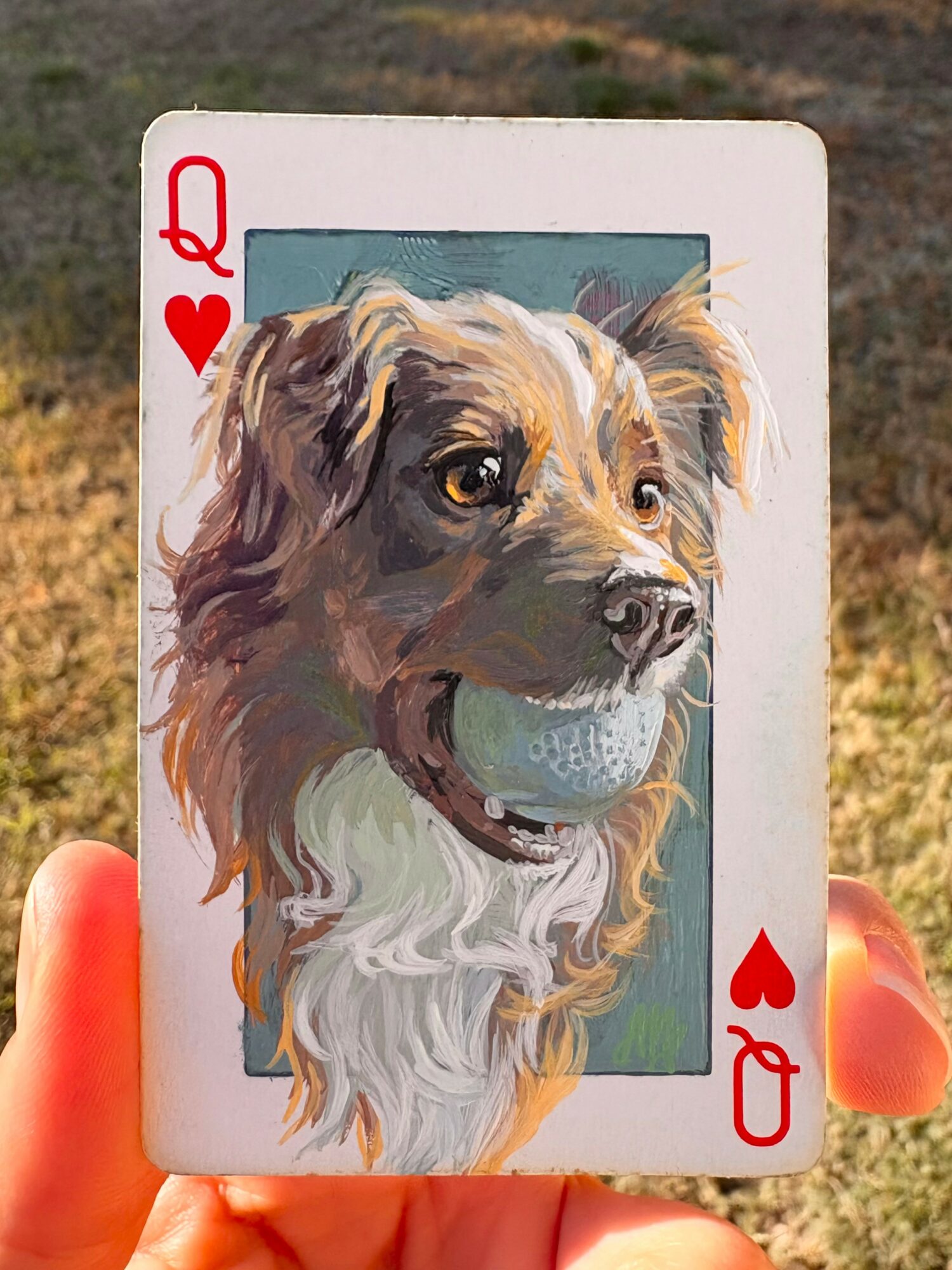 Playing card with a detailed illustration of a dog, outdoors, with a hand holding it.