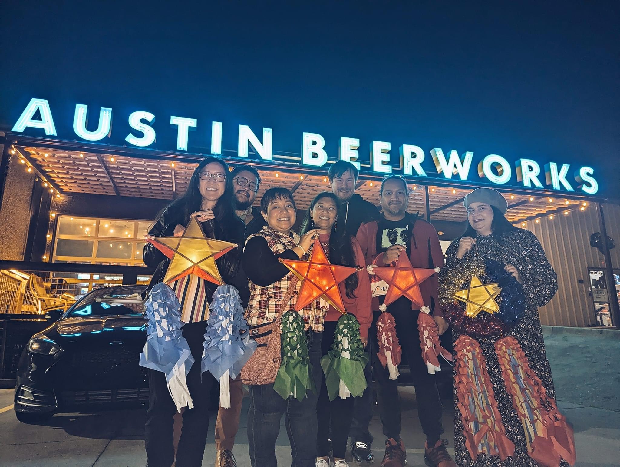Group of six people holding star-shaped lanterns outside Austin Beerworks at night.