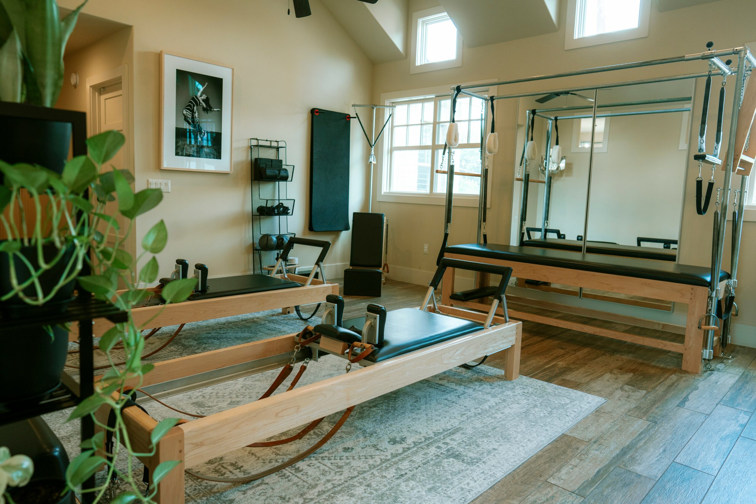 Pilates reformer machine in a bright exercise room with large windows and wooden flooring.