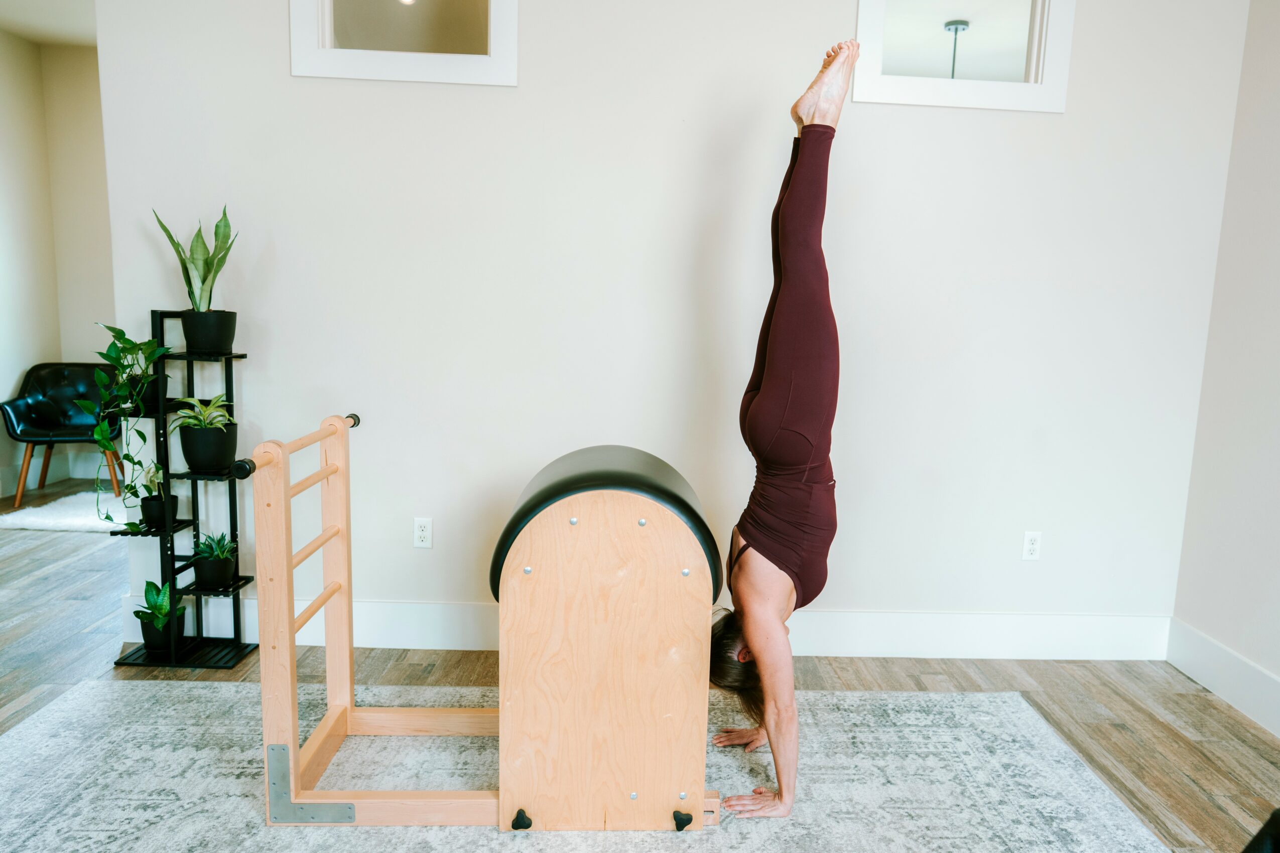 Person performing a handstand against a wall in a living room, with legs extended upward and head on the floor.
