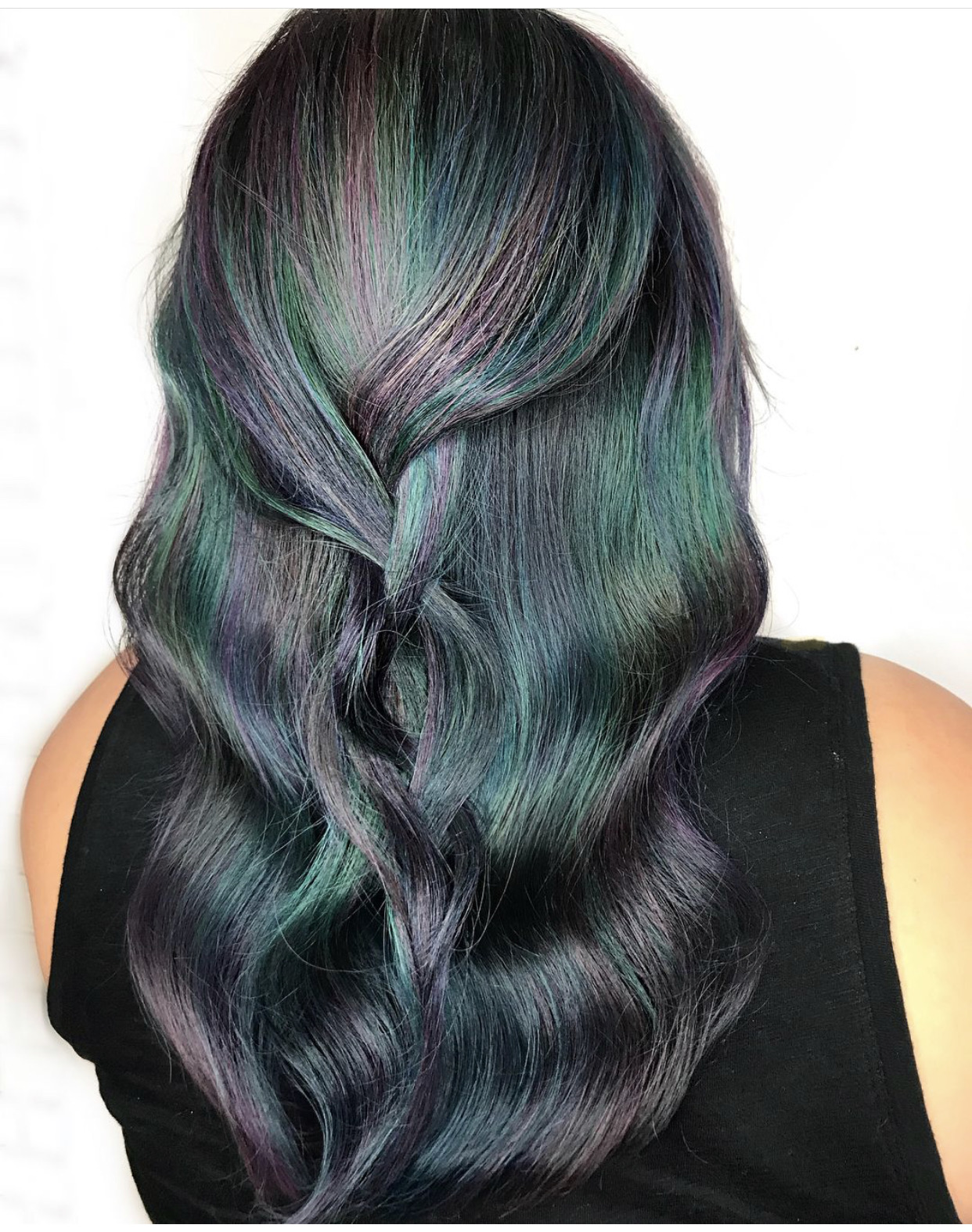 Back of a person's head with long, wavy hair in shades of black, purple, green, and blue.