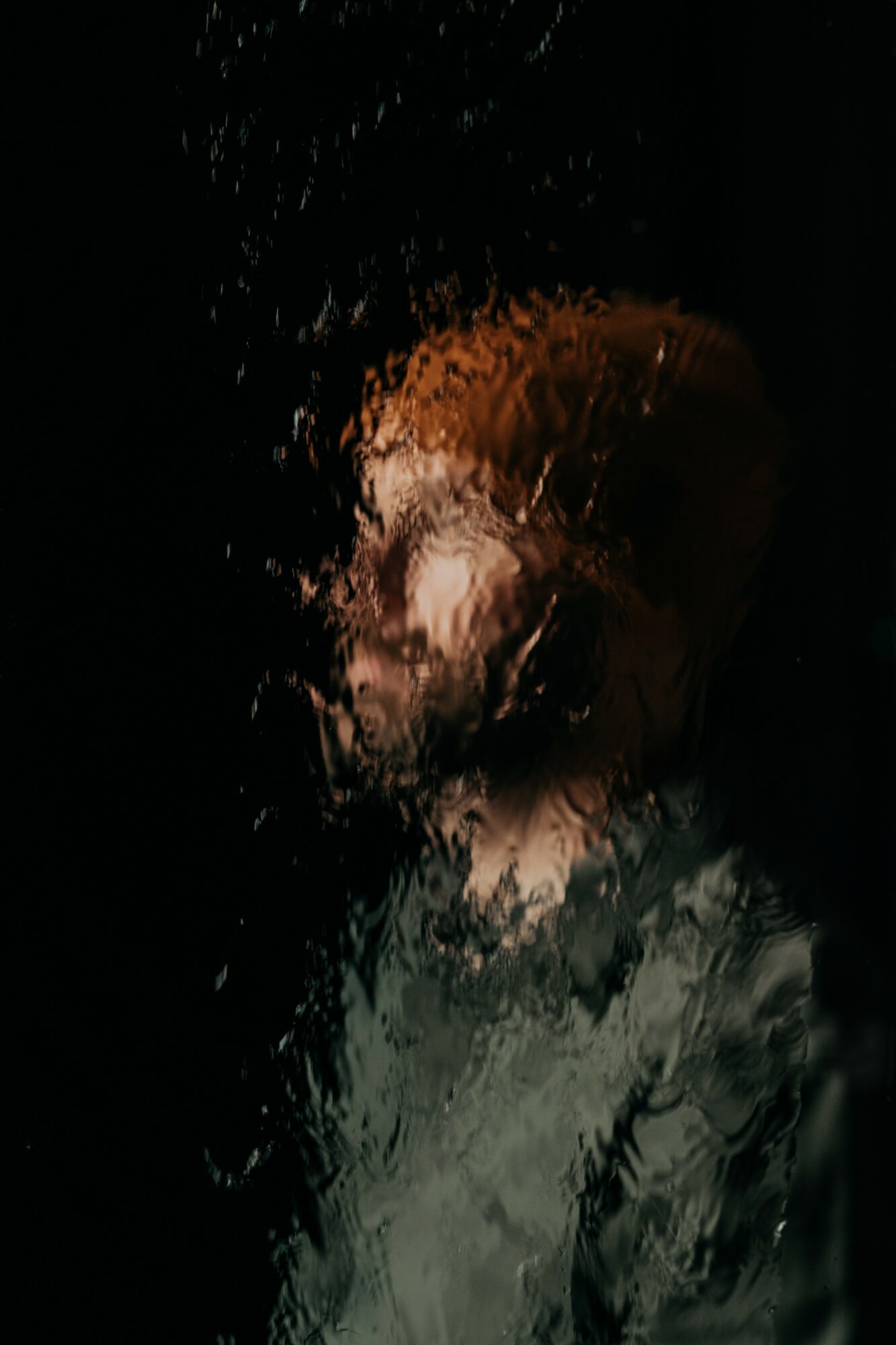 Person with short hair and a jacket, viewed through a rain-covered glass surface, obscuring details.