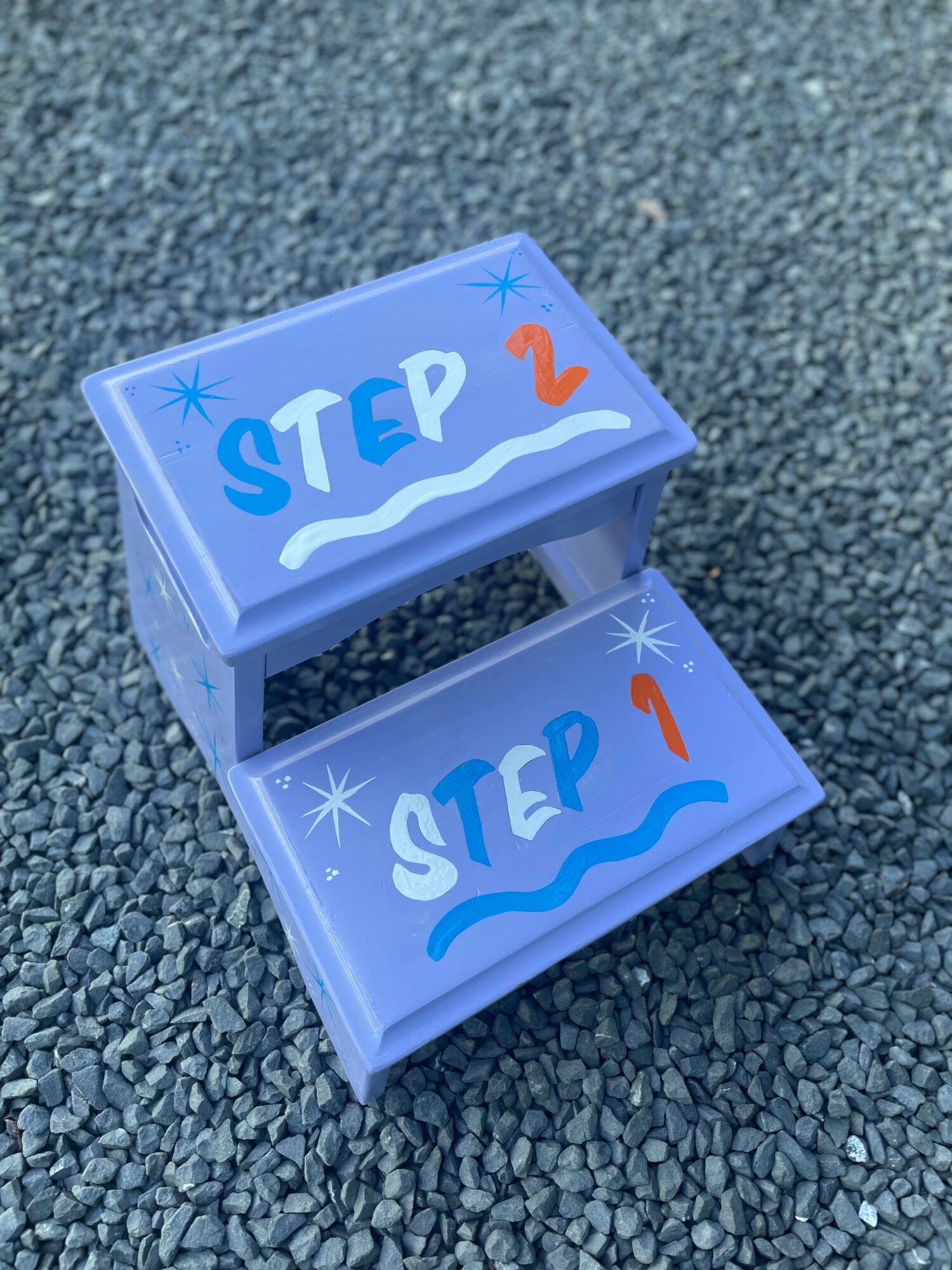 Two small blue steps with painted text 'STEP 2' and 'STEP 1' on a gravel surface.