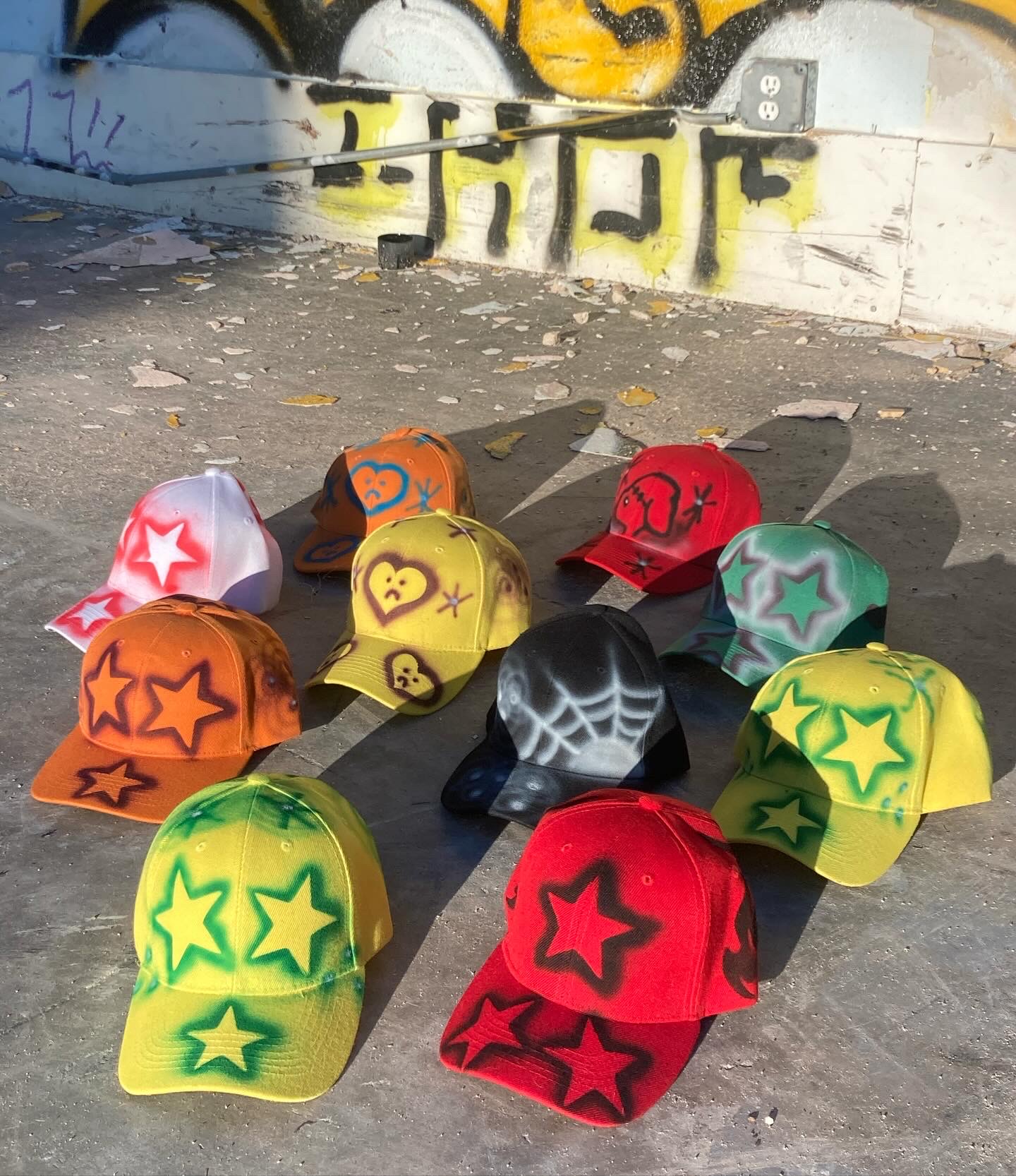 Nine colorful caps with star designs arranged on the ground in front of a graffiti wall.