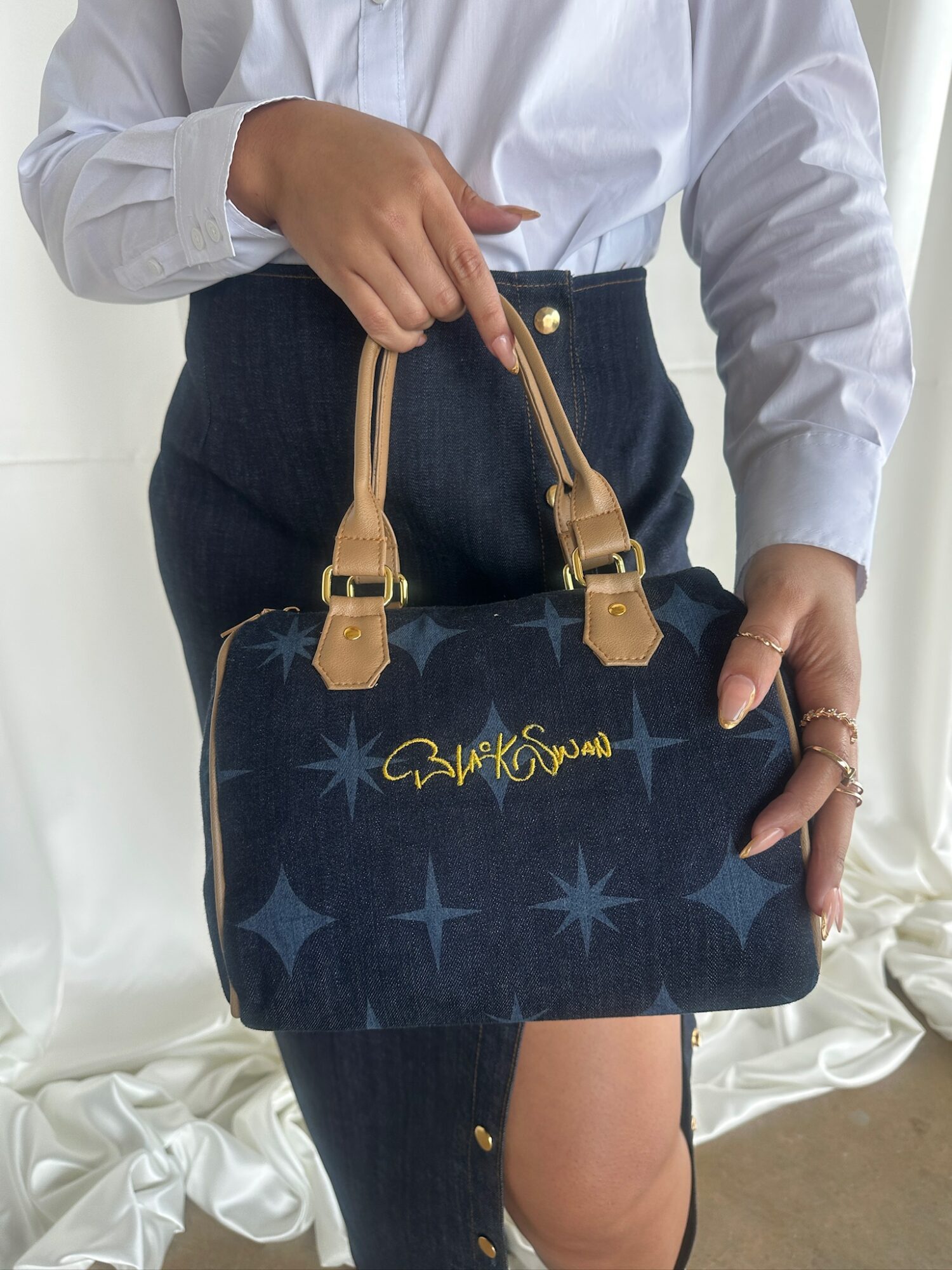 Person holding a dark blue designer handbag with gold accents and star patterns, wearing a white shirt and dark pants.