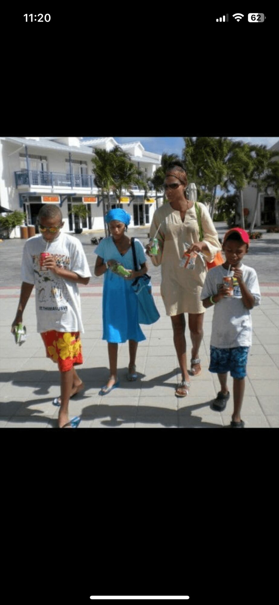 Four people walking outdoors on a sunny day, with buildings and palm trees in the background.