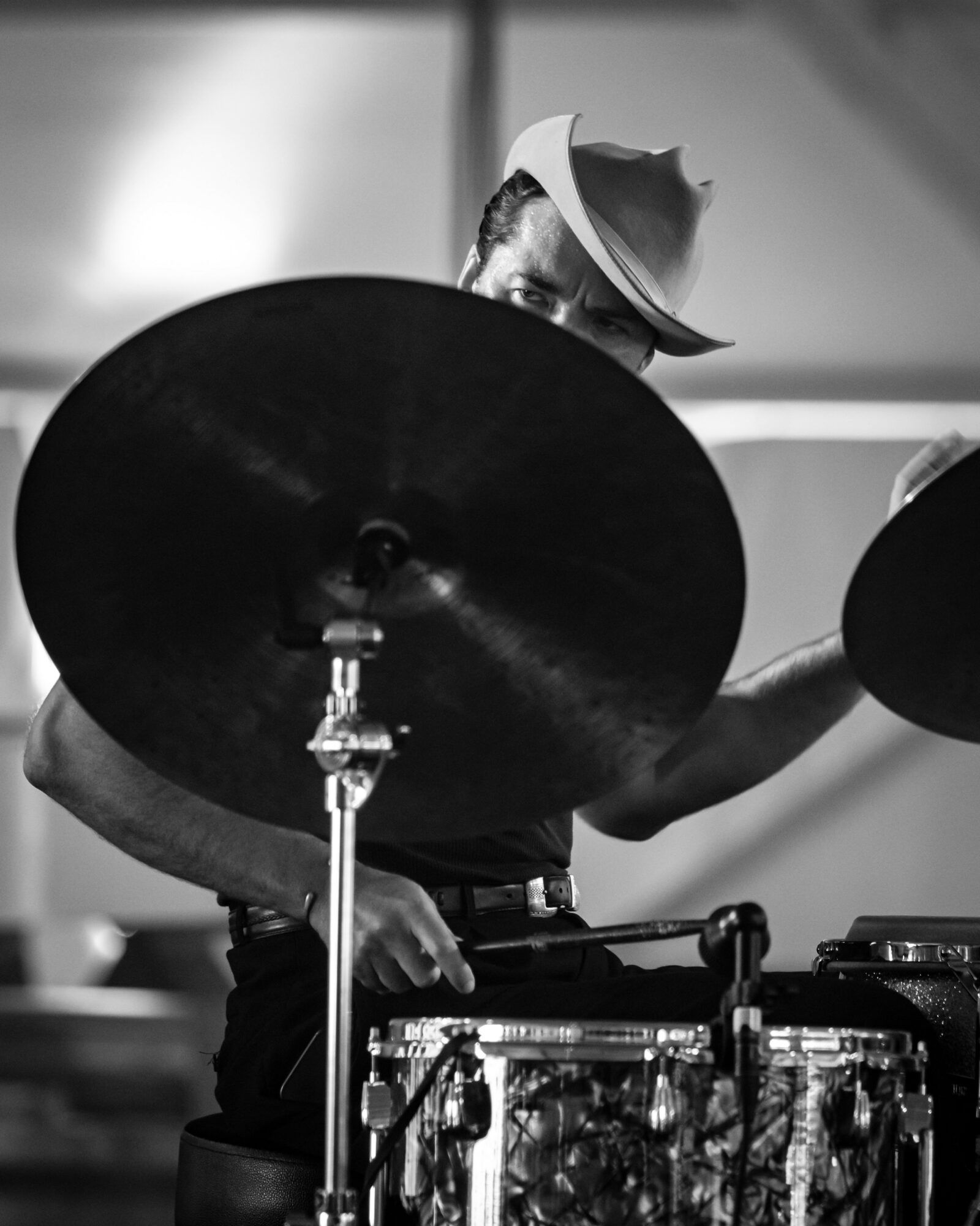 Child playing drums with cymbals, wearing a hat, in a room with blurred background.