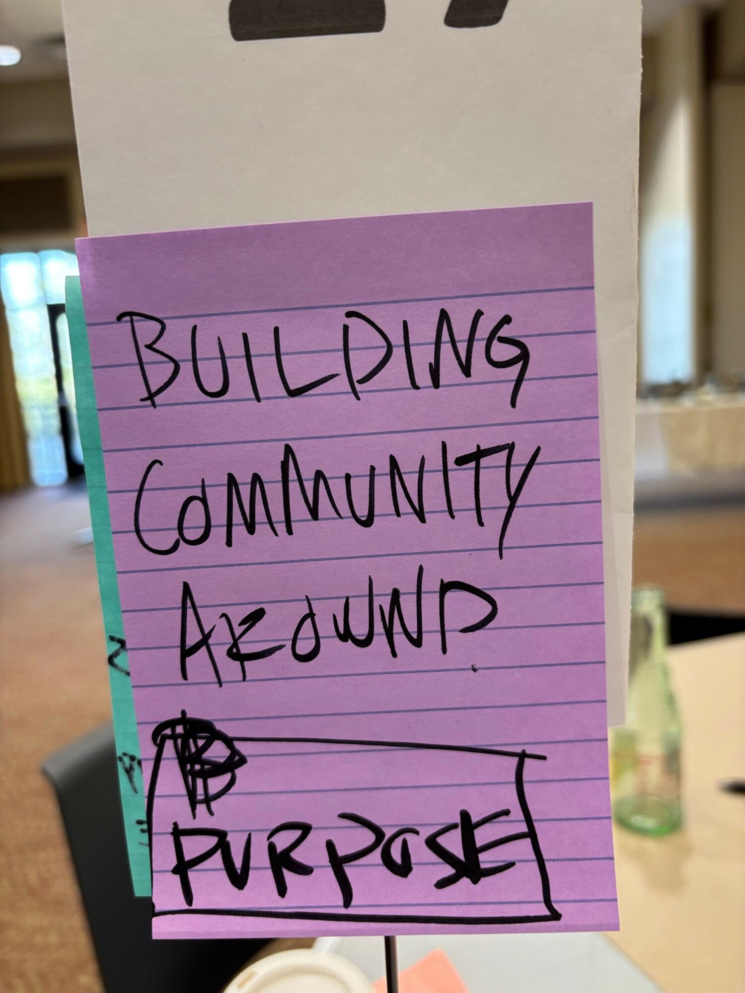 Purple sticky note with handwritten text about building community and a small drawing of a house.