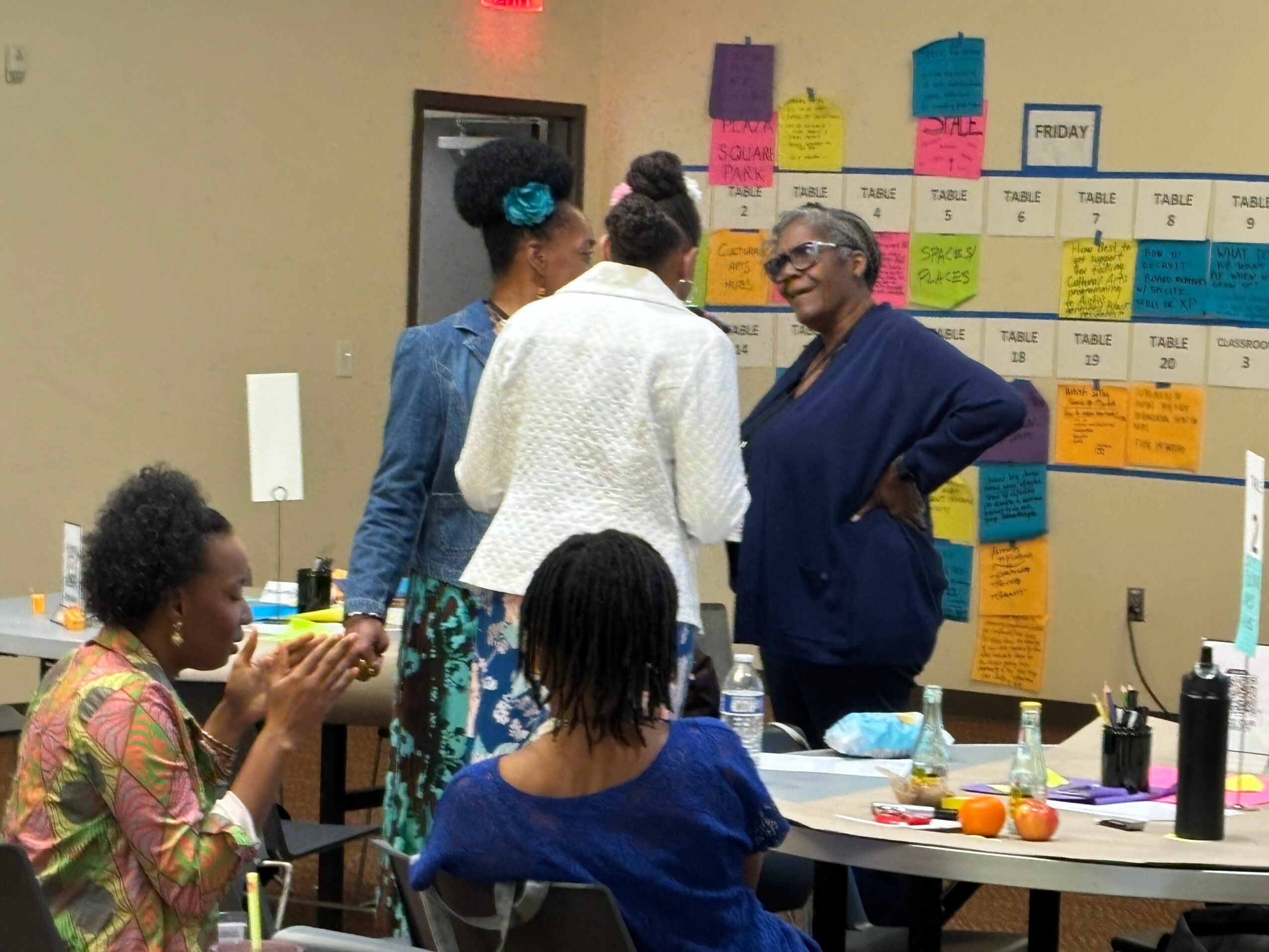 Group of people engaged in discussion in a room with colorful sticky notes on the wall.