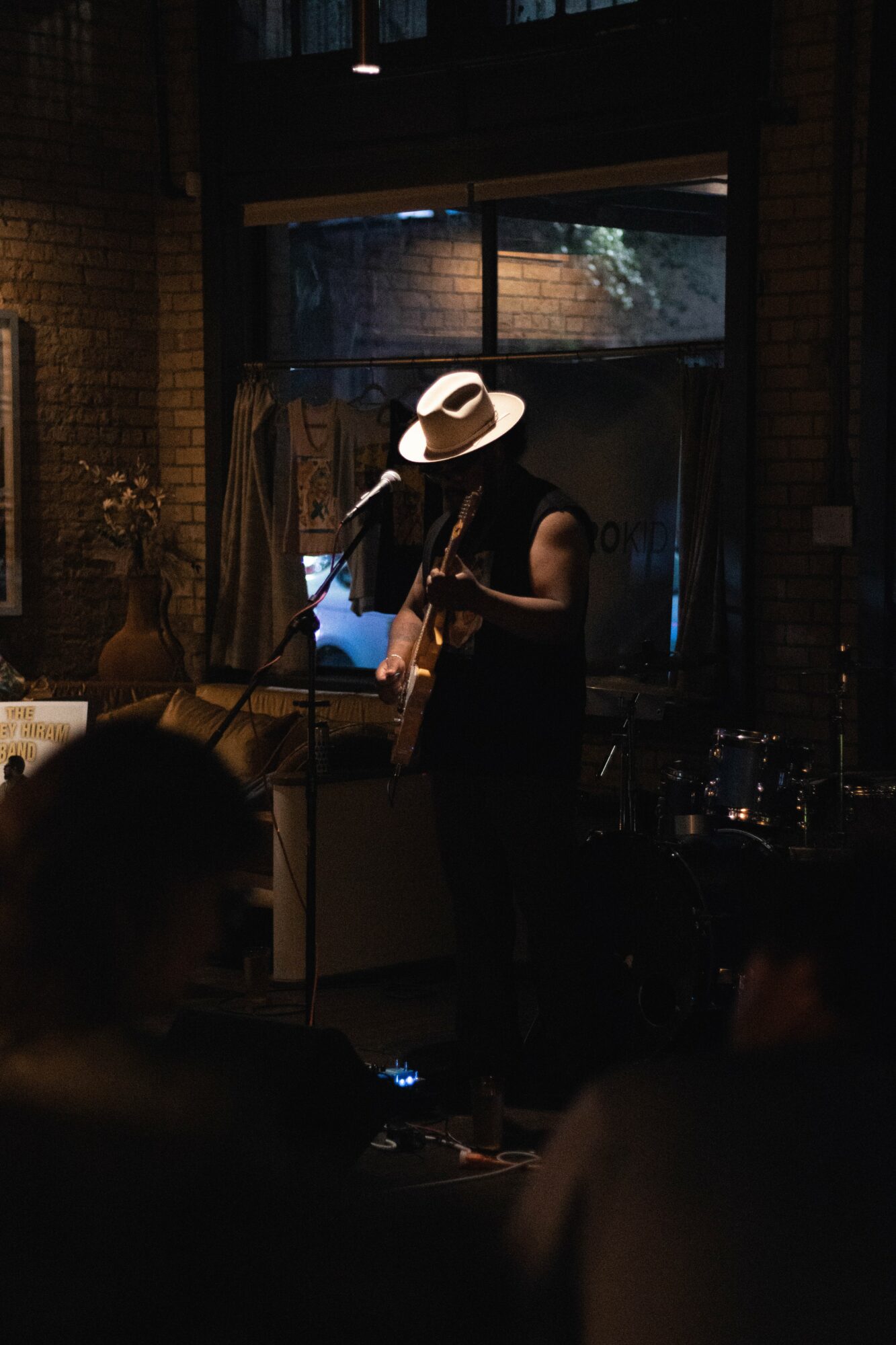 Person wearing a hat playing guitar on stage in a dimly lit venue.