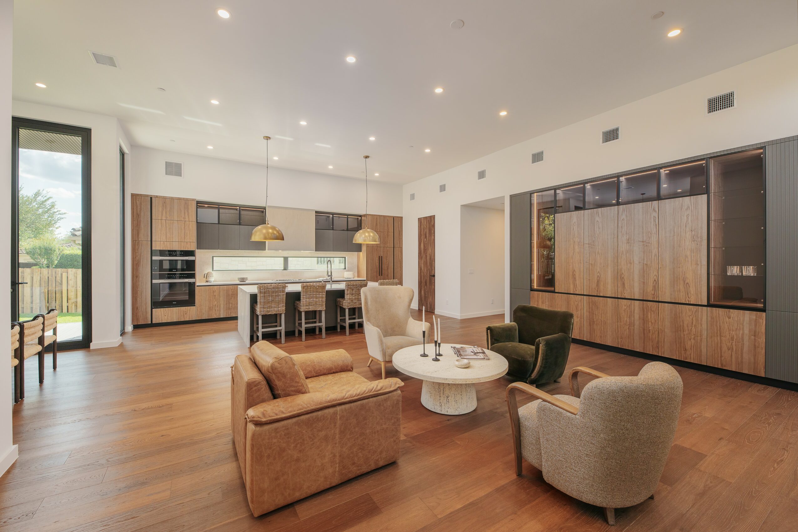 Open-concept living room and kitchen with wooden flooring, modern furniture, and large windows, bright and spacious interior.